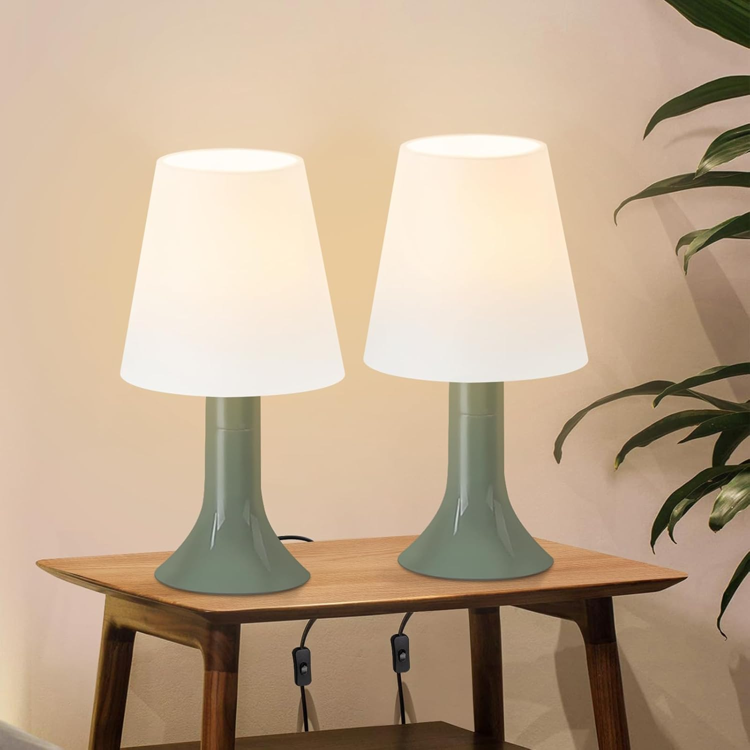 Dwie lampy z białymi kloszami i zielonymi podstawami stoją na drewnianym stole. Widoczne są czarne przewody.