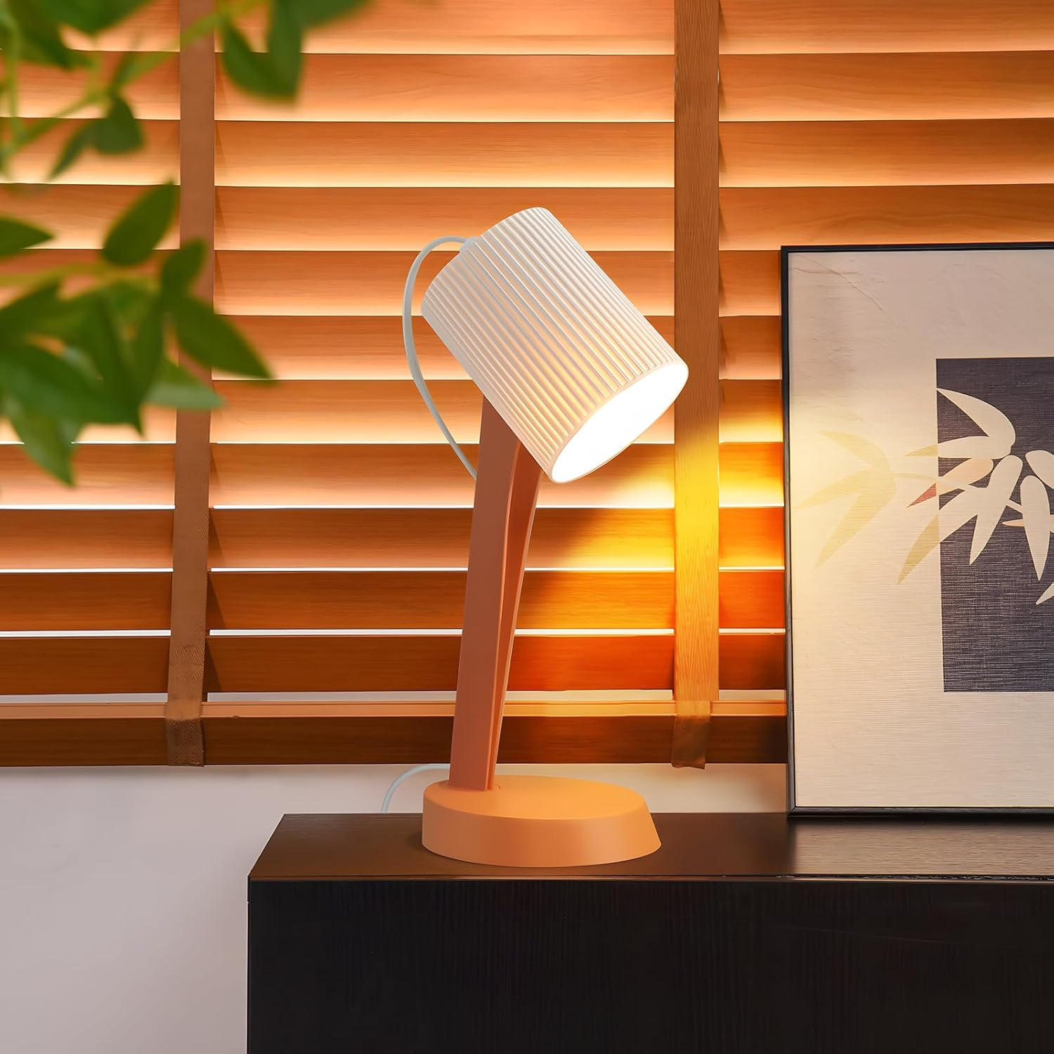 Lampa biurkowa z pomarańczową podstawą i trzonem. Lampa ma biały, cylindryczny klosz.