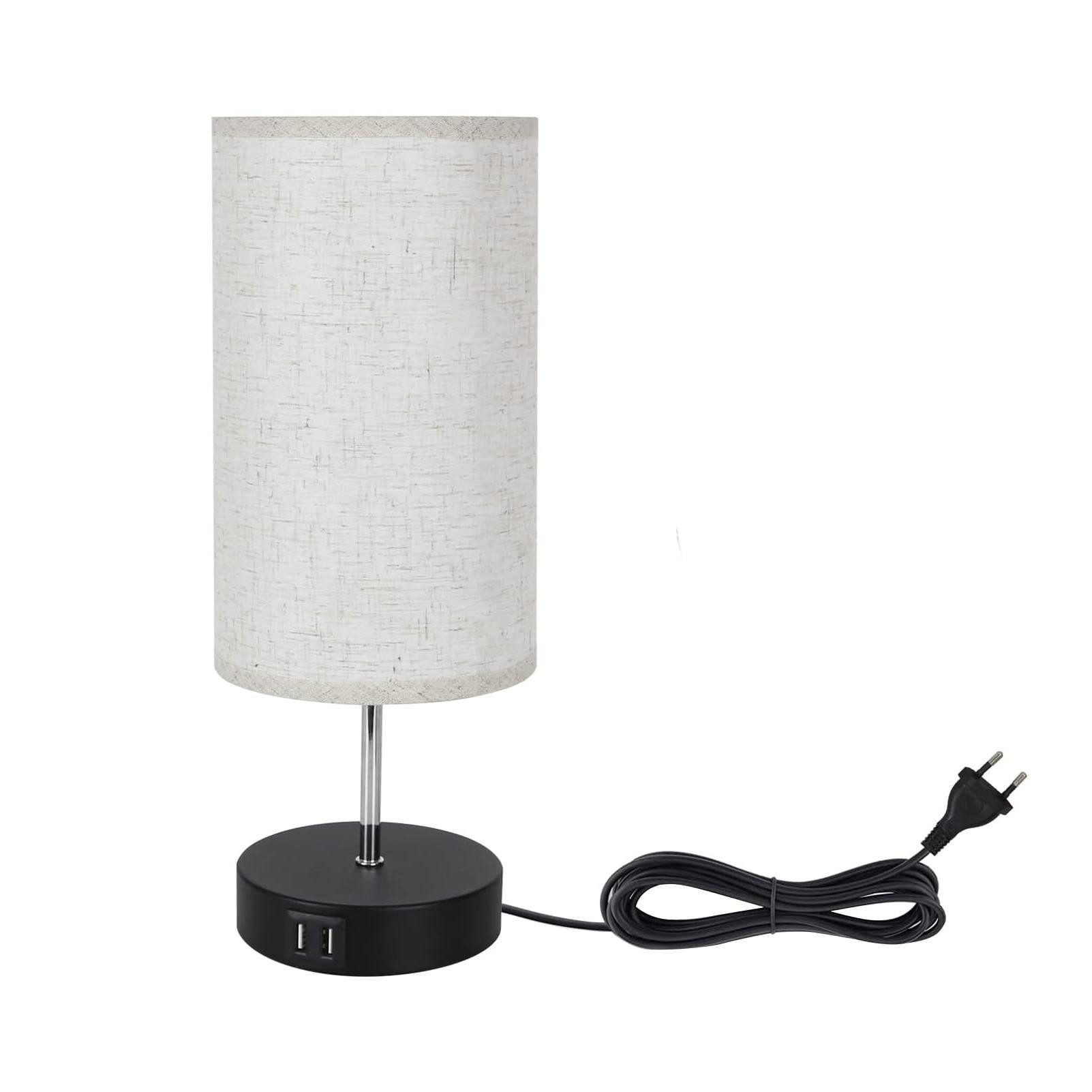 Una lampada da tavolo bianca con paralume cilindrico e base nera, collegata a una presa a muro con un cavo nero.
