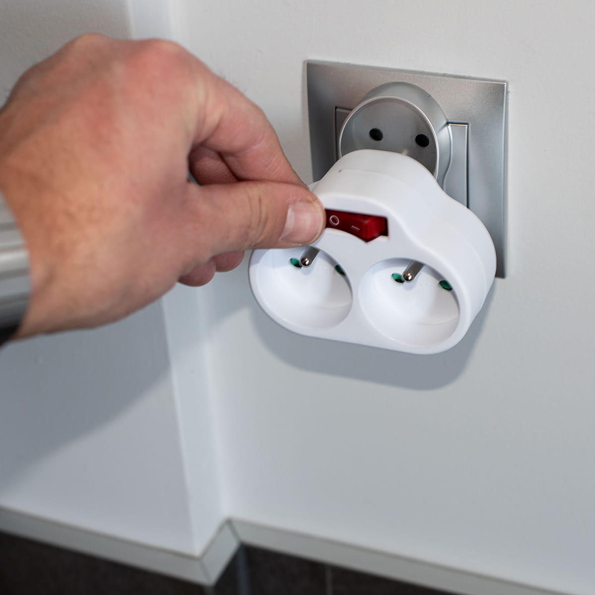 Ręka dotyka biały adapter z czerwonym przełącznikiem wpięty do gniazdka.