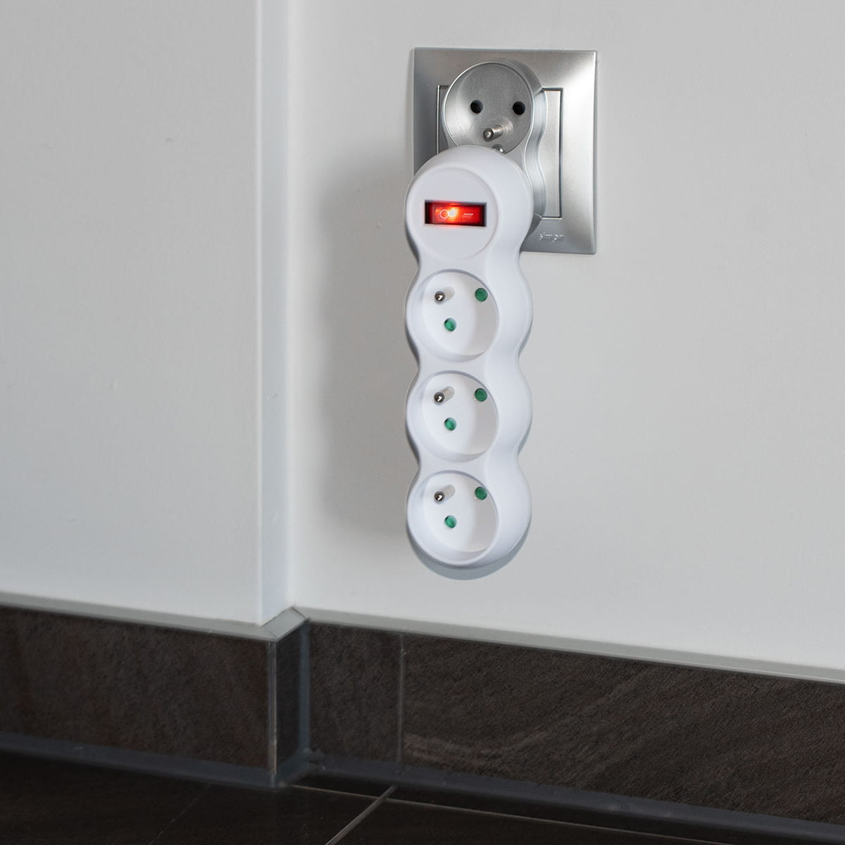 Biała listwa zasilająca z czterema gniazdami, wpięta w ścianę. Ma czerwony włącznik.