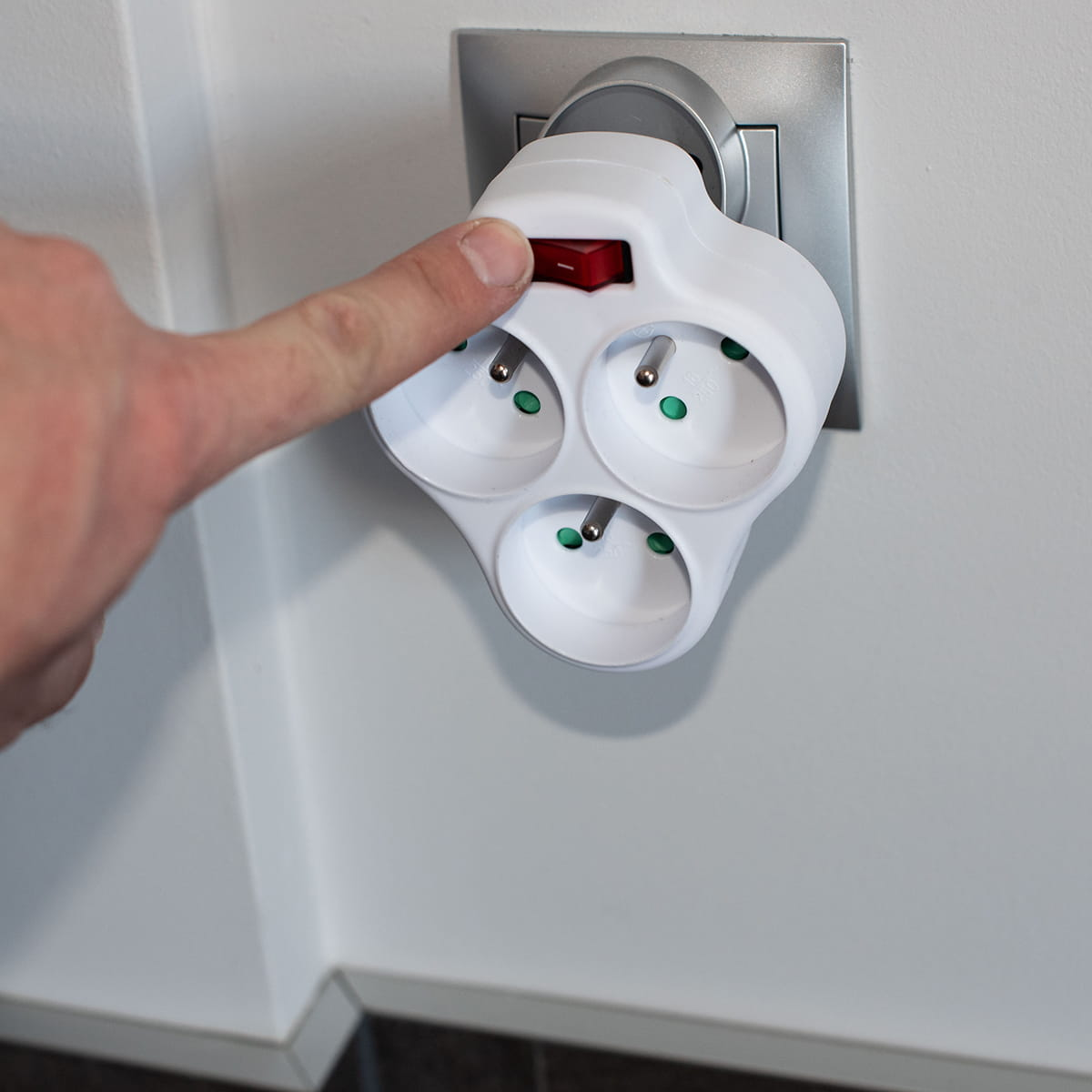 Palec naciska czerwony włącznik białego potrójnego gniazda.