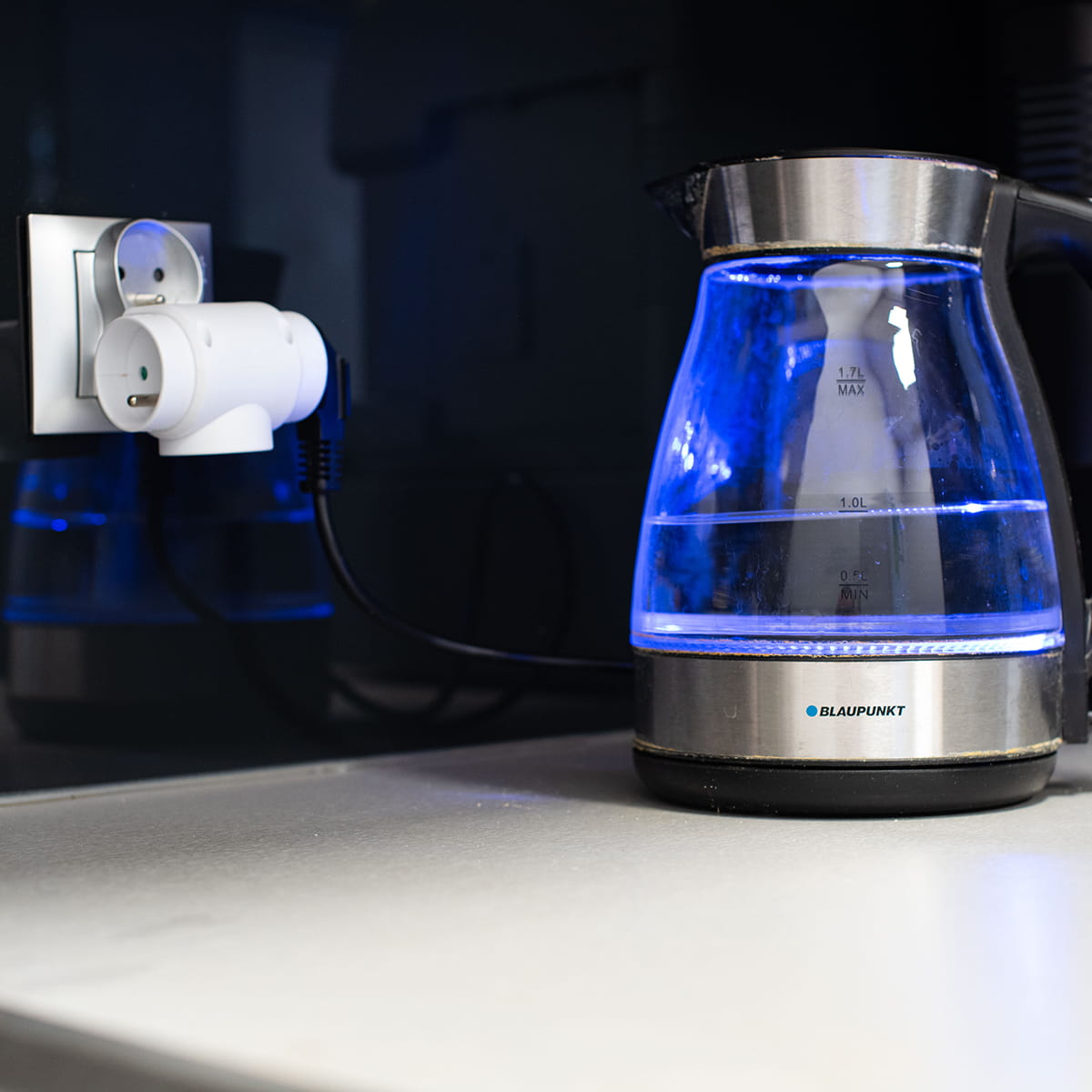 Czajnik podłączony do potrójnego gniazda. Czajnik i gniazdo na białej powierzchni.