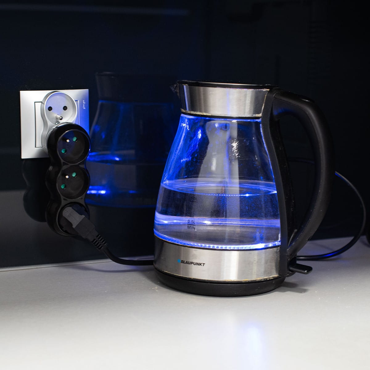 Biały potrójny adapter z podłączonym czajnikiem, z niebieskim światłem.