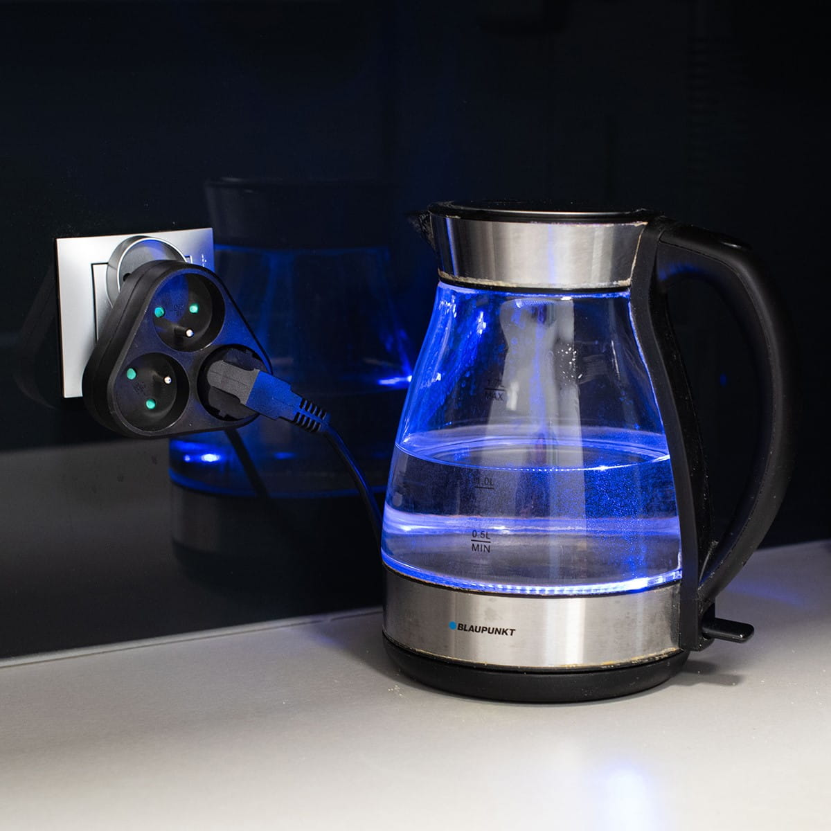 Czajnik i adapter zasilania na blacie. Czajnik ma niebieskie światło. Adapter ma podłączony kabel.