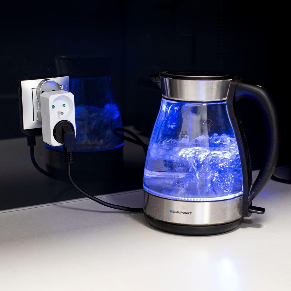 Czajnik z niebieskim światłem, podłączony do białego adaptera, który jest w gniazdku ściennym.