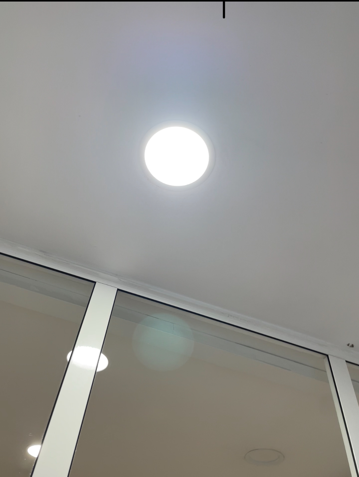 Mirando hacia arriba a un techo blanco con una luminaria circular. Debajo, una pared de vidrio.