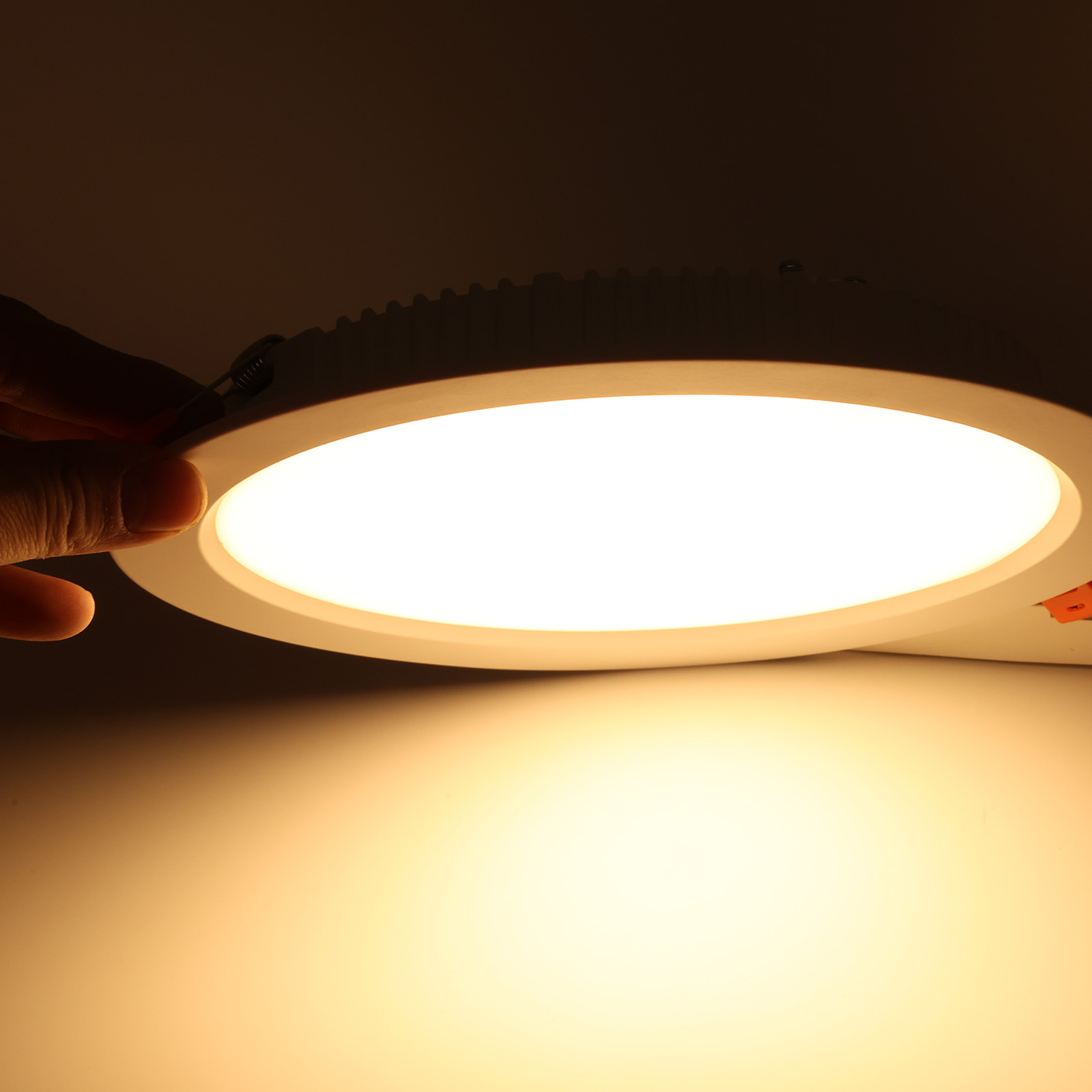 Mano tocando una luz LED blanca, iluminando con un brillo cálido y amarillo. Clip naranja visible.