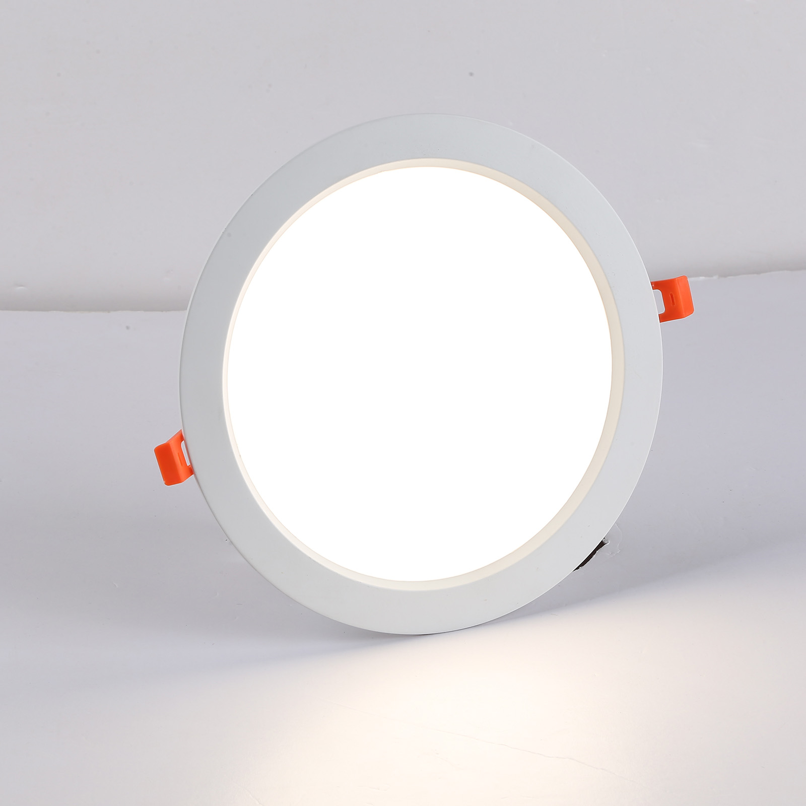 Luz LED redonda blanca sobre una superficie blanca. La luz tiene clips naranjas.