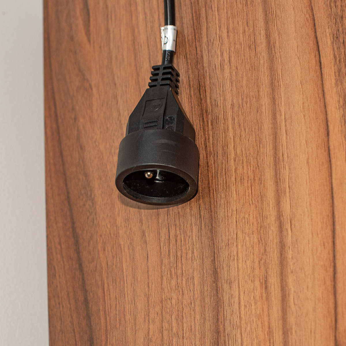 Czarne gniazdo jest wpięte w drewnianą powierzchnię. Tło to gładka ściana.