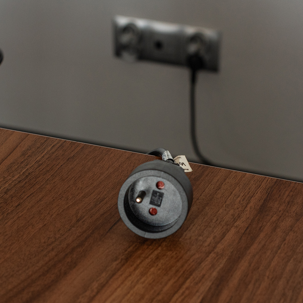 Czarne gniazdo z dwoma czerwonymi kropkami na brązowej drewnianej powierzchni. Drugie rozmyte.