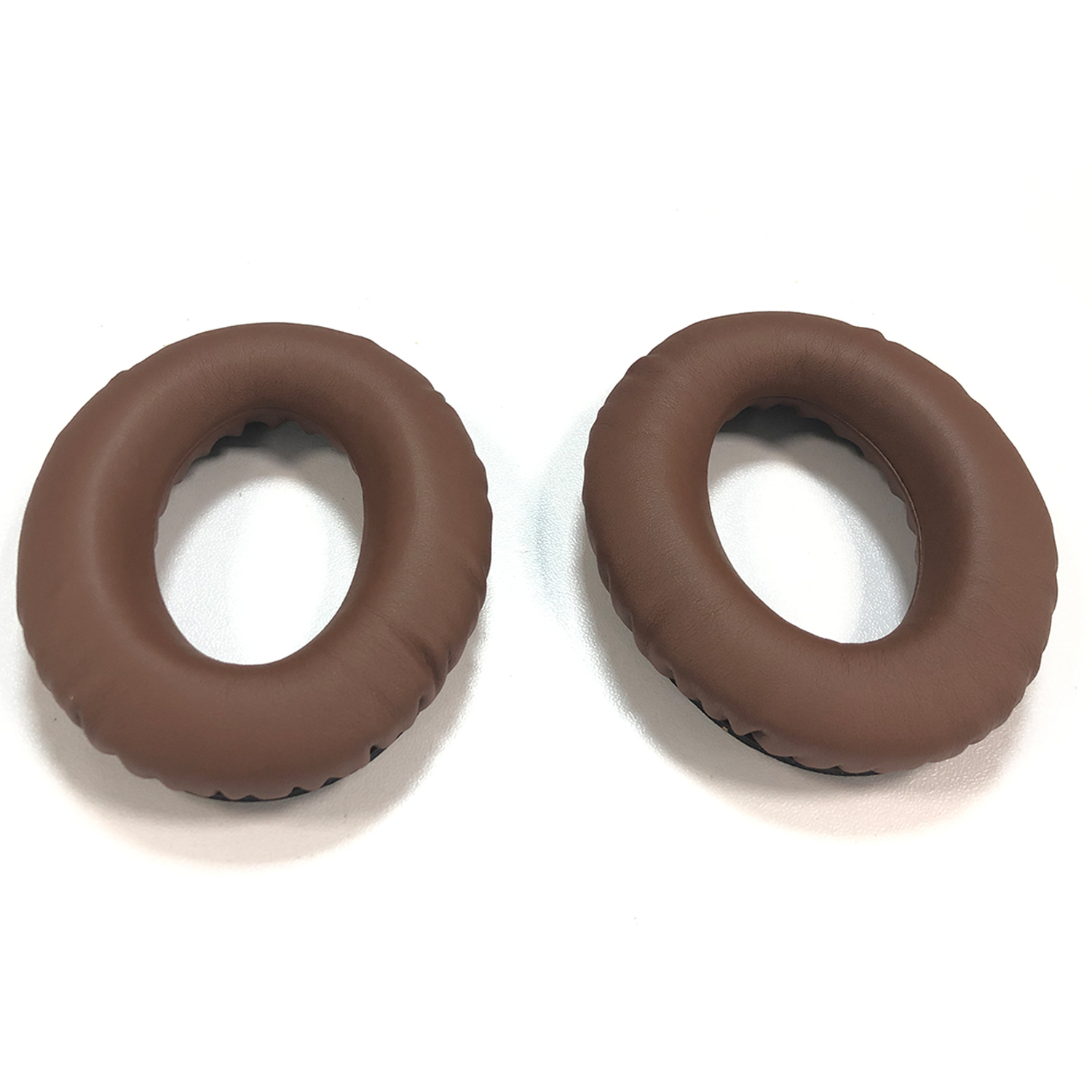 Dwie brązowe poduszki nauszne do słuchawek. Białe tło.