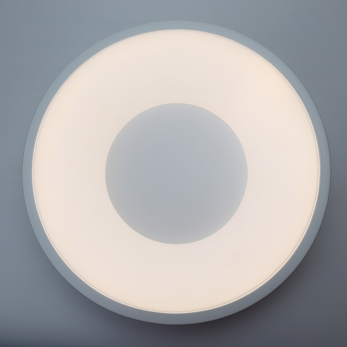 Una lámpara de techo circular, brillantemente iluminada, contra un techo blanco.