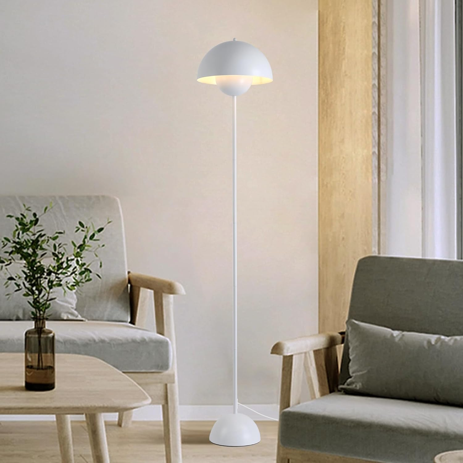 Lámpara de pie blanca con pantalla de cúpula, junto a sillas y un jarrón en un salón con luz solar.