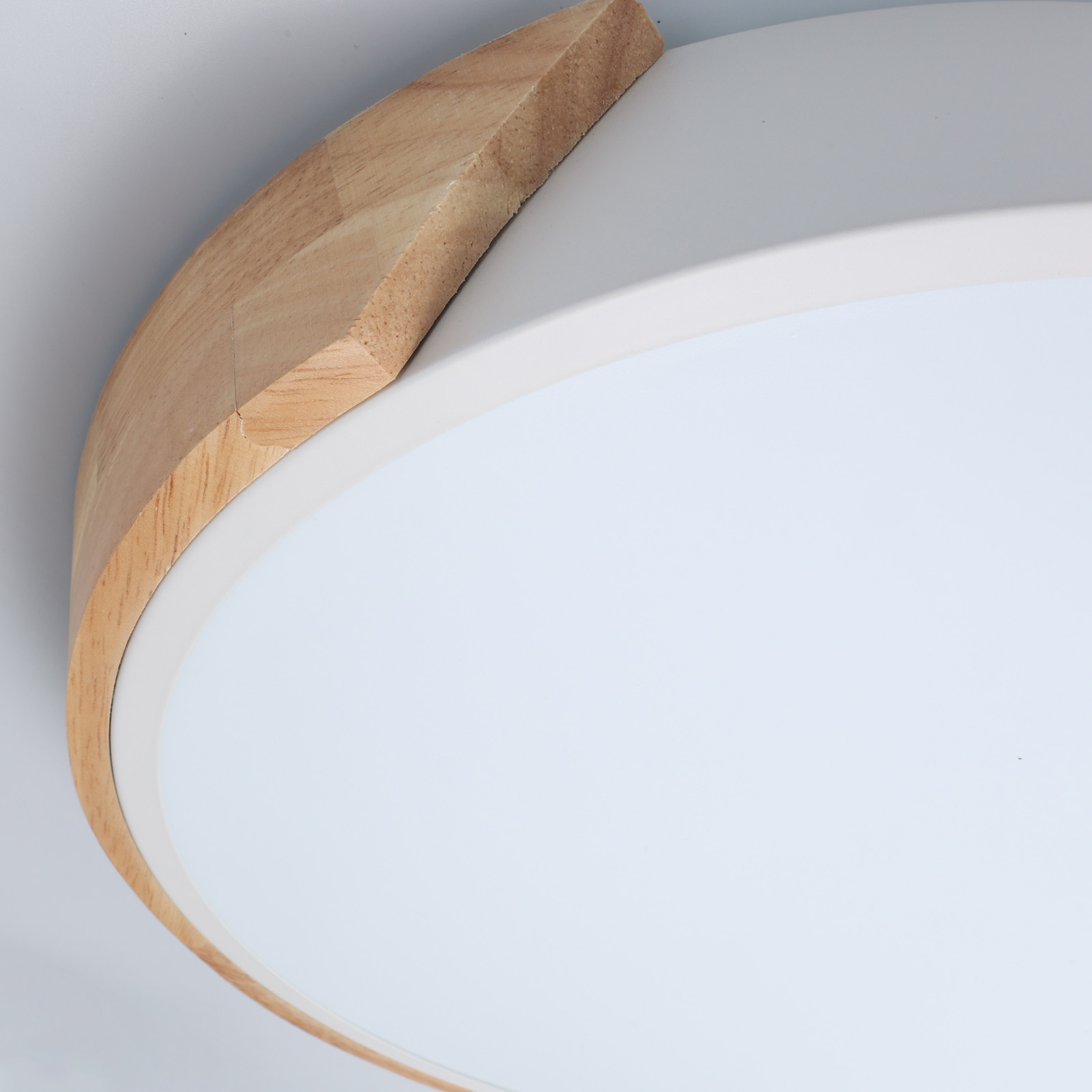 Primer plano del borde de madera y el centro blanco de una lámpara de techo. La luz tiene un diseño moderno.