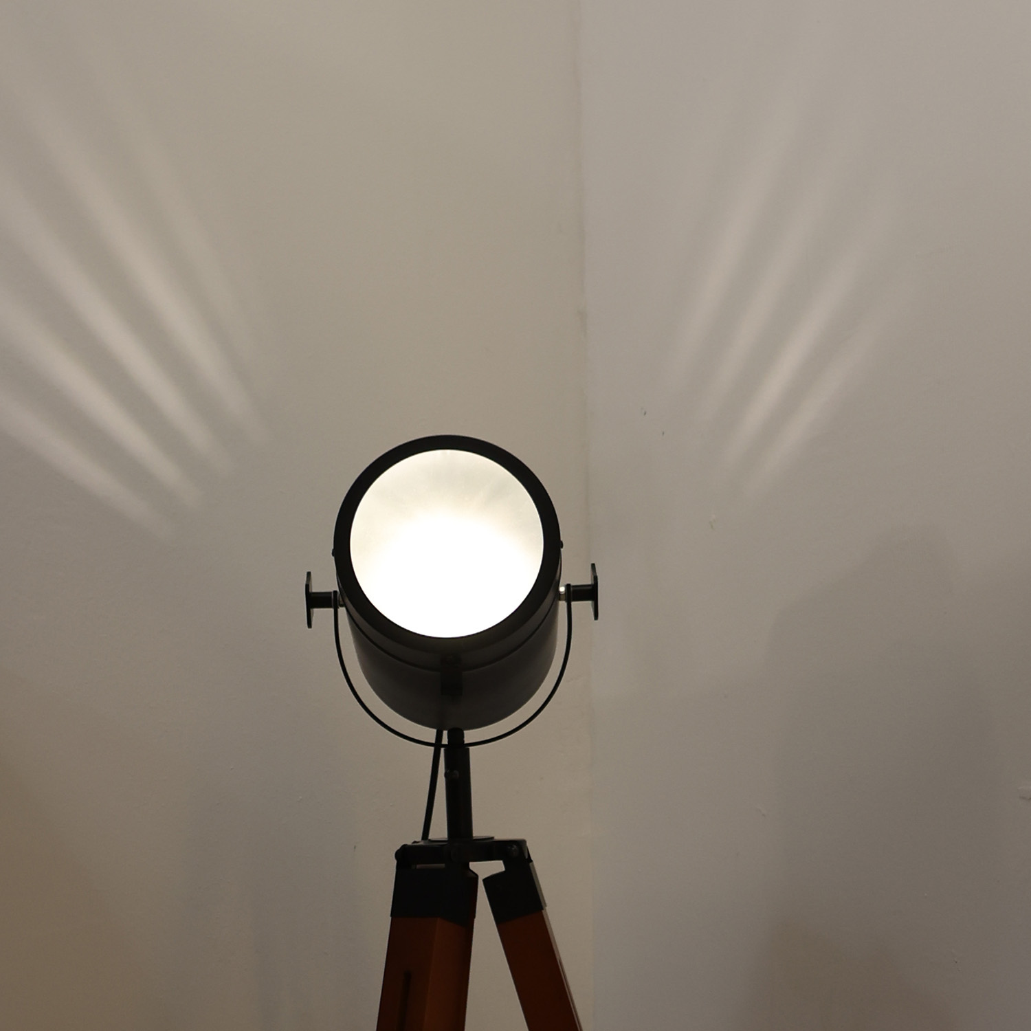 Un foco negro está brillando. Está sobre un trípode. La luz brilla sobre una pared blanca.