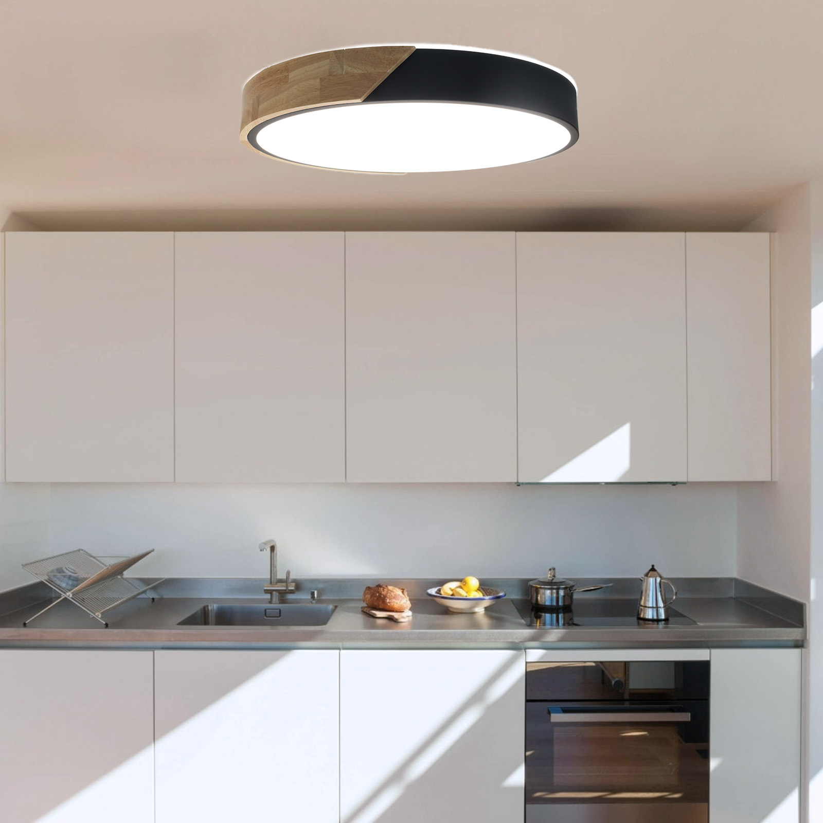 Cocina con una lámpara de techo redonda. La lámpara tiene secciones de madera y negras. Armarios blancos y encimera acero inox.