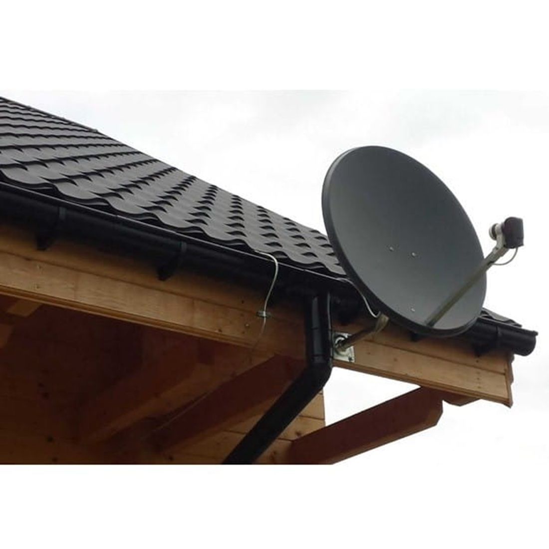Antena satelitarna na dachu. Talerz jest czarny, a dach ma ciemne gonty. Widoczna jest drewniana konstrukcja.