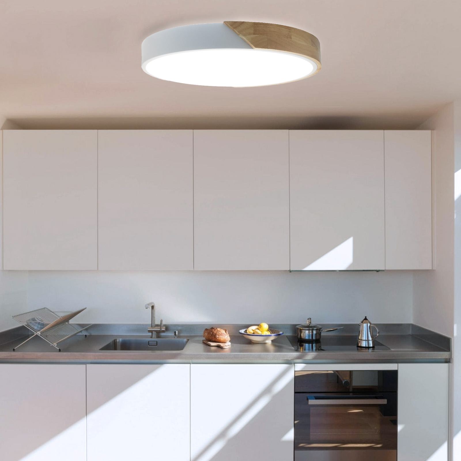 Una escena de cocina con una lámpara de techo, gabinetes blancos y encimeras de acero inoxidable, con comida.