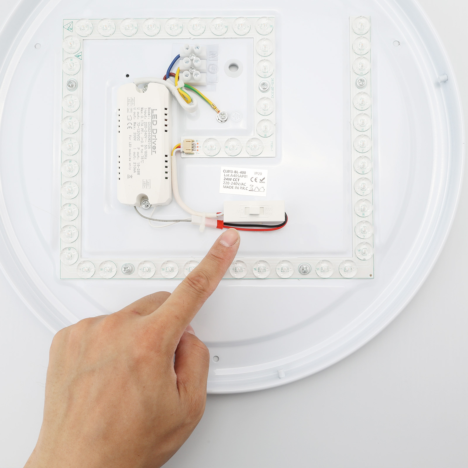 Primer plano de una mano que señala el interior de una lámpara de techo LED redonda y blanca.