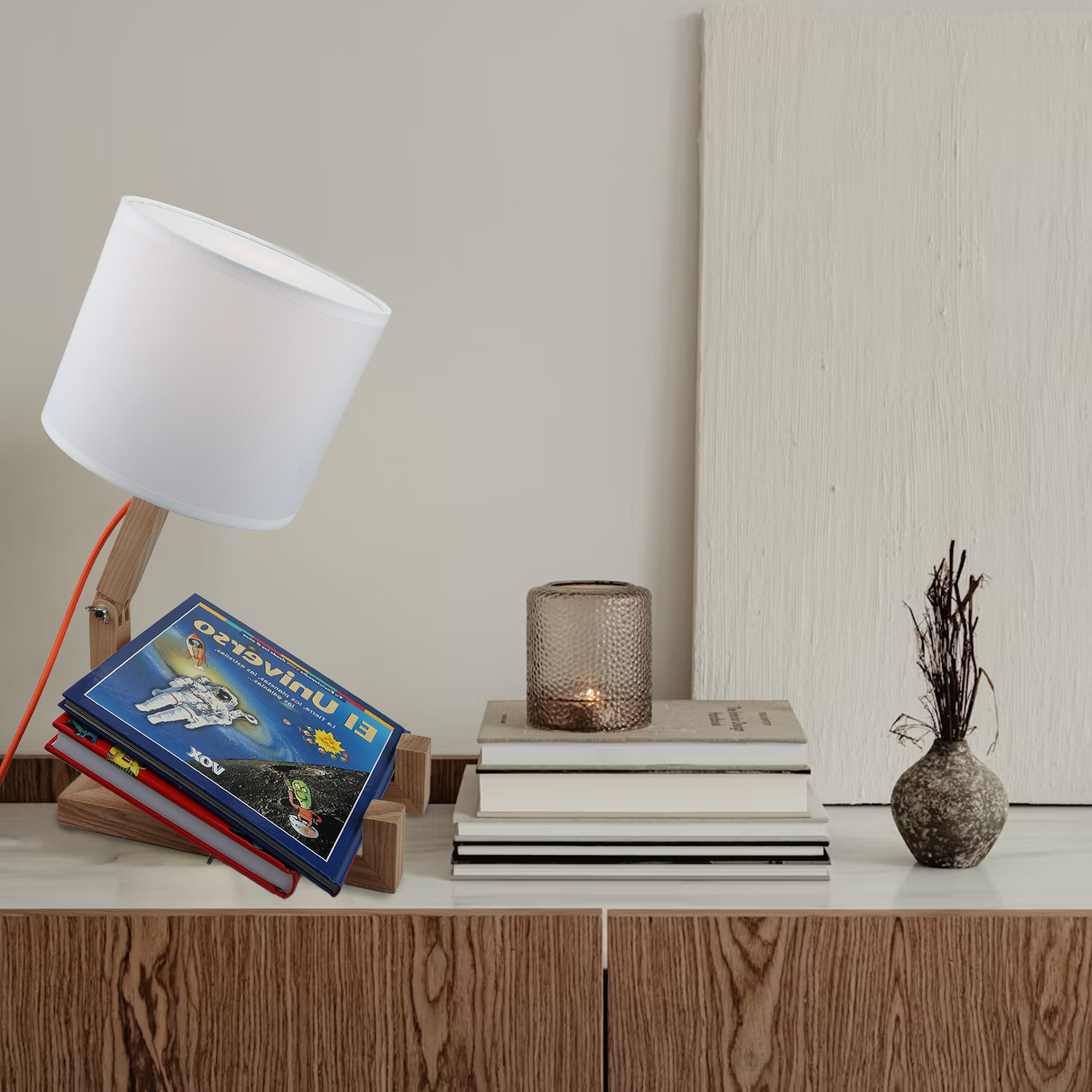 Lámpara de escritorio de madera con pantalla blanca, libros, vela y jarrón sobre superficie blanca.
