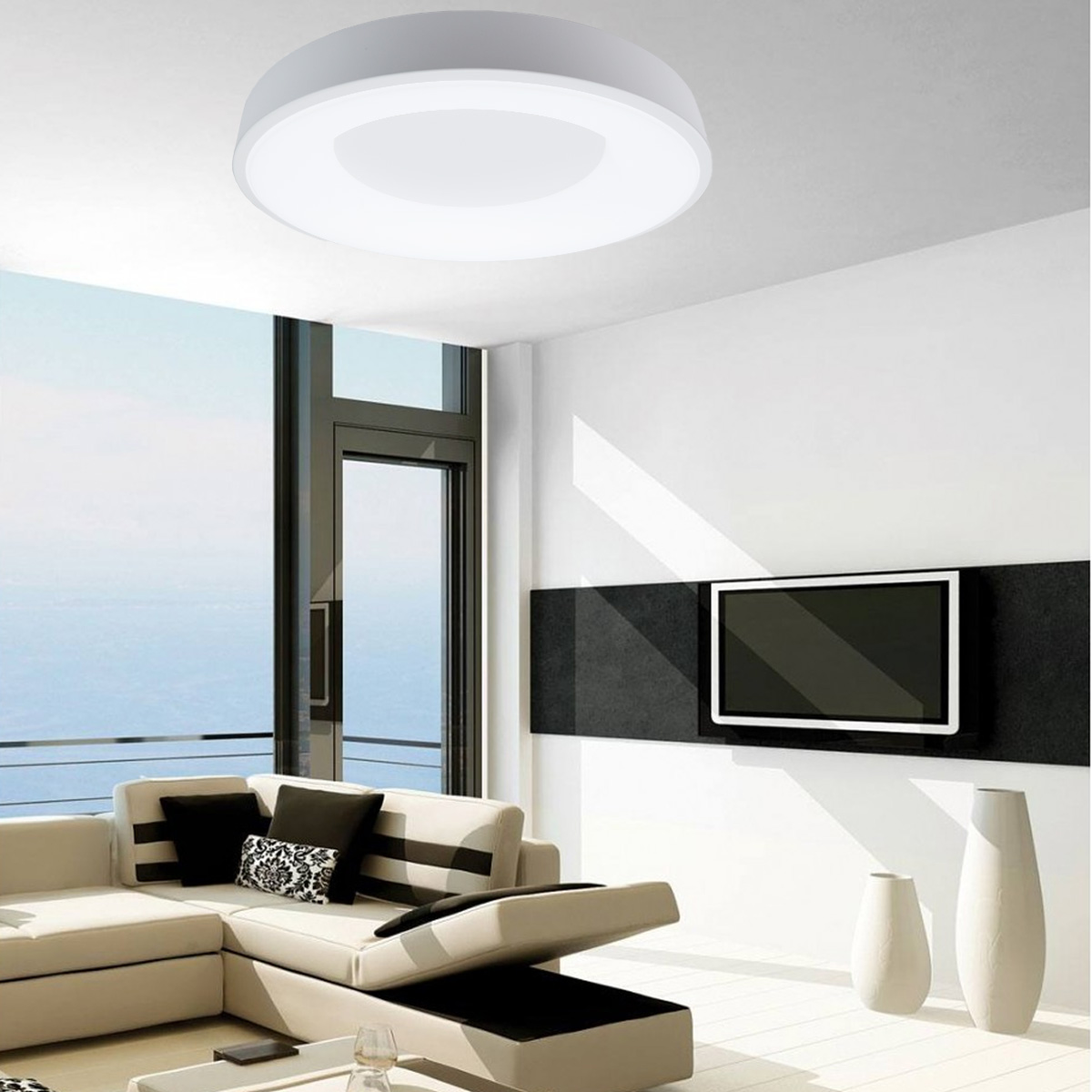 Una lámpara de techo redonda blanca en una habitación moderna. La habitación tiene un sofá, televisor y ventana grande.