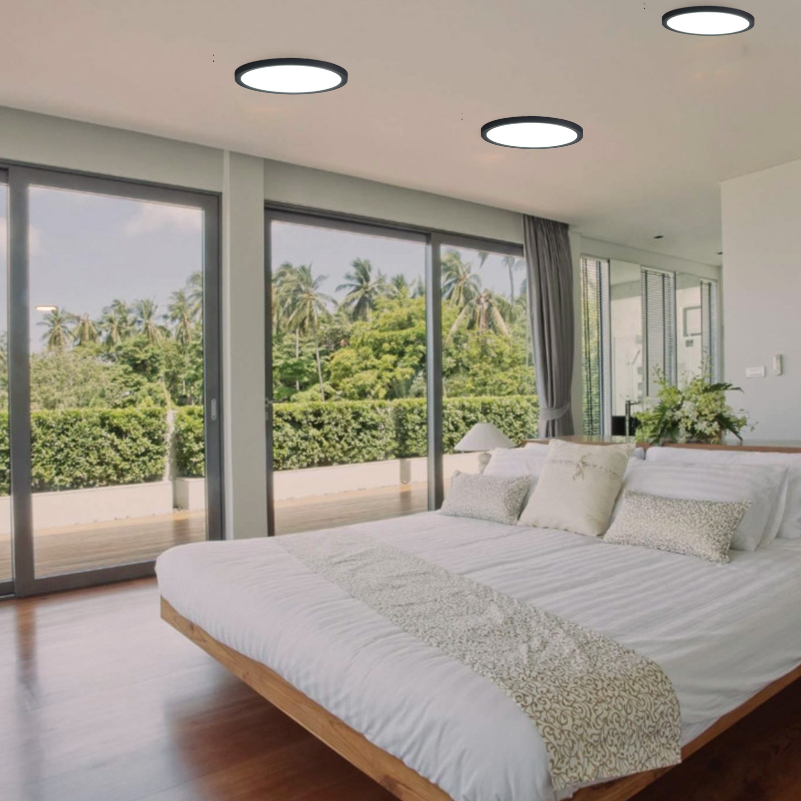 Dormitorio con grandes ventanales con vistas a un paisaje verde. Tres luces de techo negras sobre la cama.