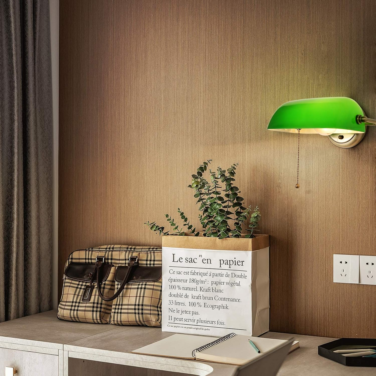 Una lámpara de pared verde sobre una mesa con objetos, junto a una pared con bolsa de papel.