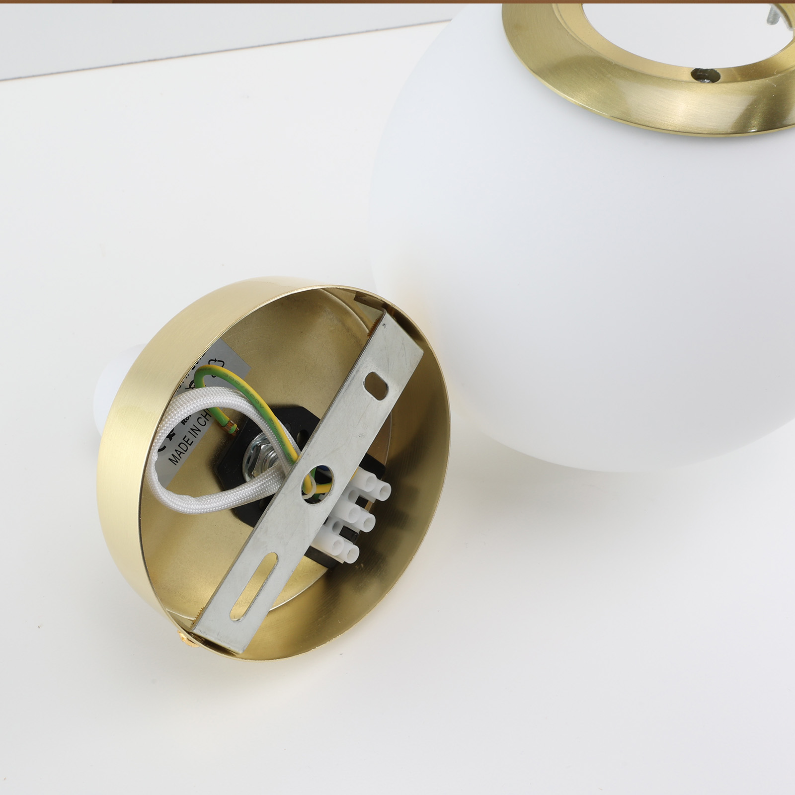 Primer plano de una lámpara globo blanca, con base dorada y cableado.