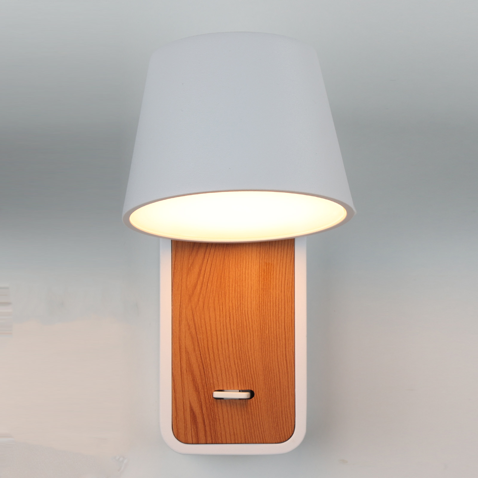 Una lámpara de pared con una pantalla blanca. La lámpara está montada en una pared de madera y blanca.