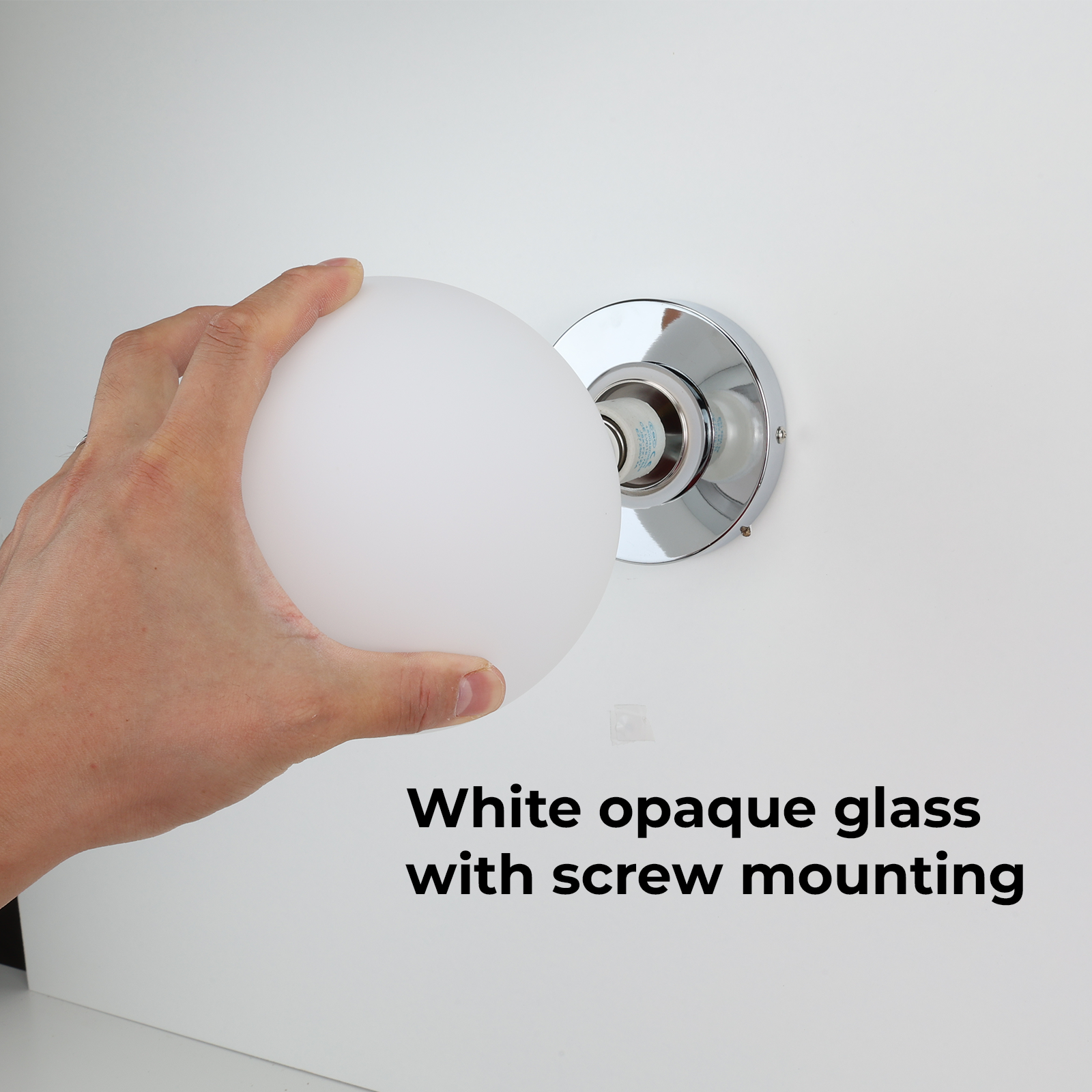 Una mano sosteniendo un globo blanco junto a una lámpara de pared con base cromada.