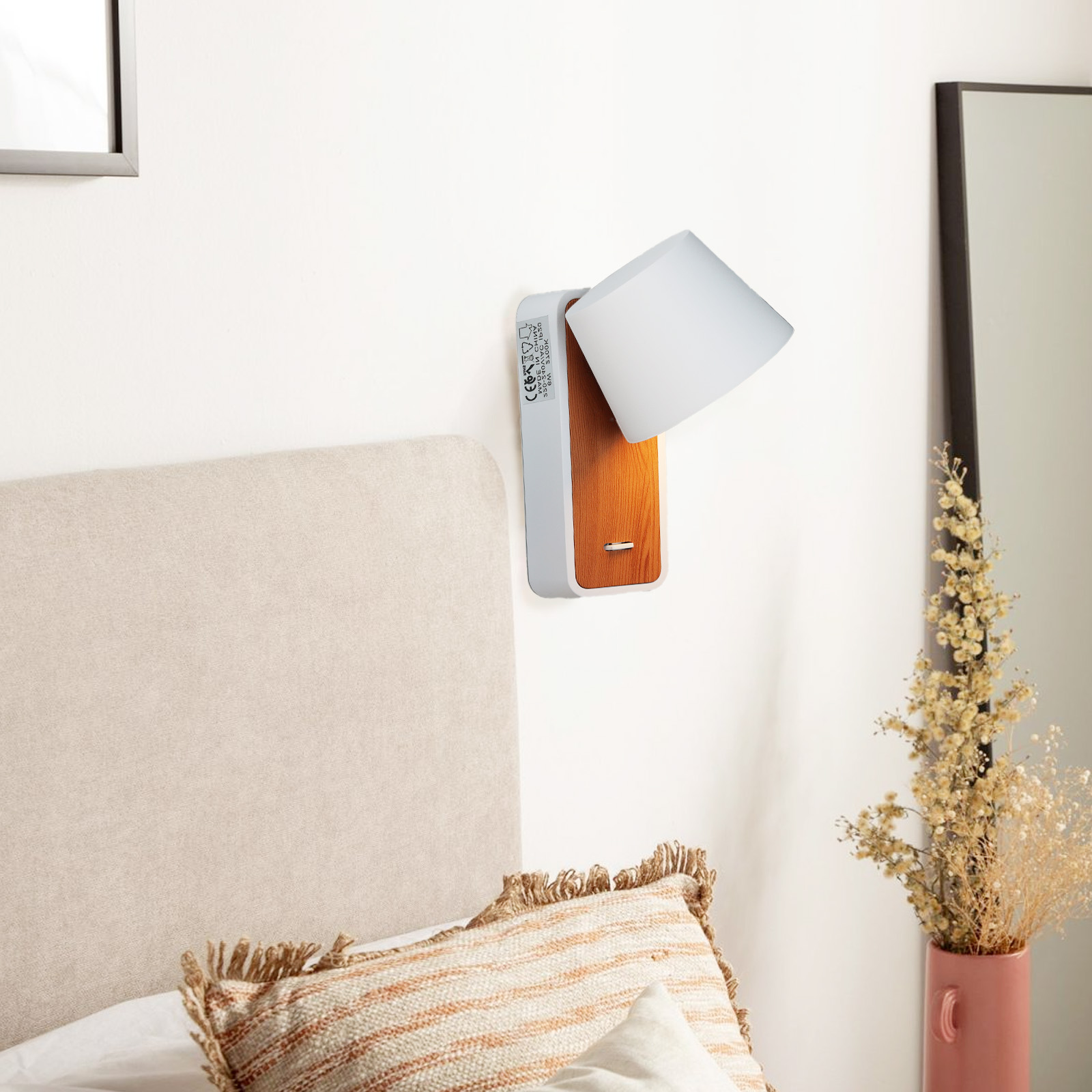 Una lámpara de pared con una pantalla blanca y base de madera está montada en una pared blanca junto a una cama.