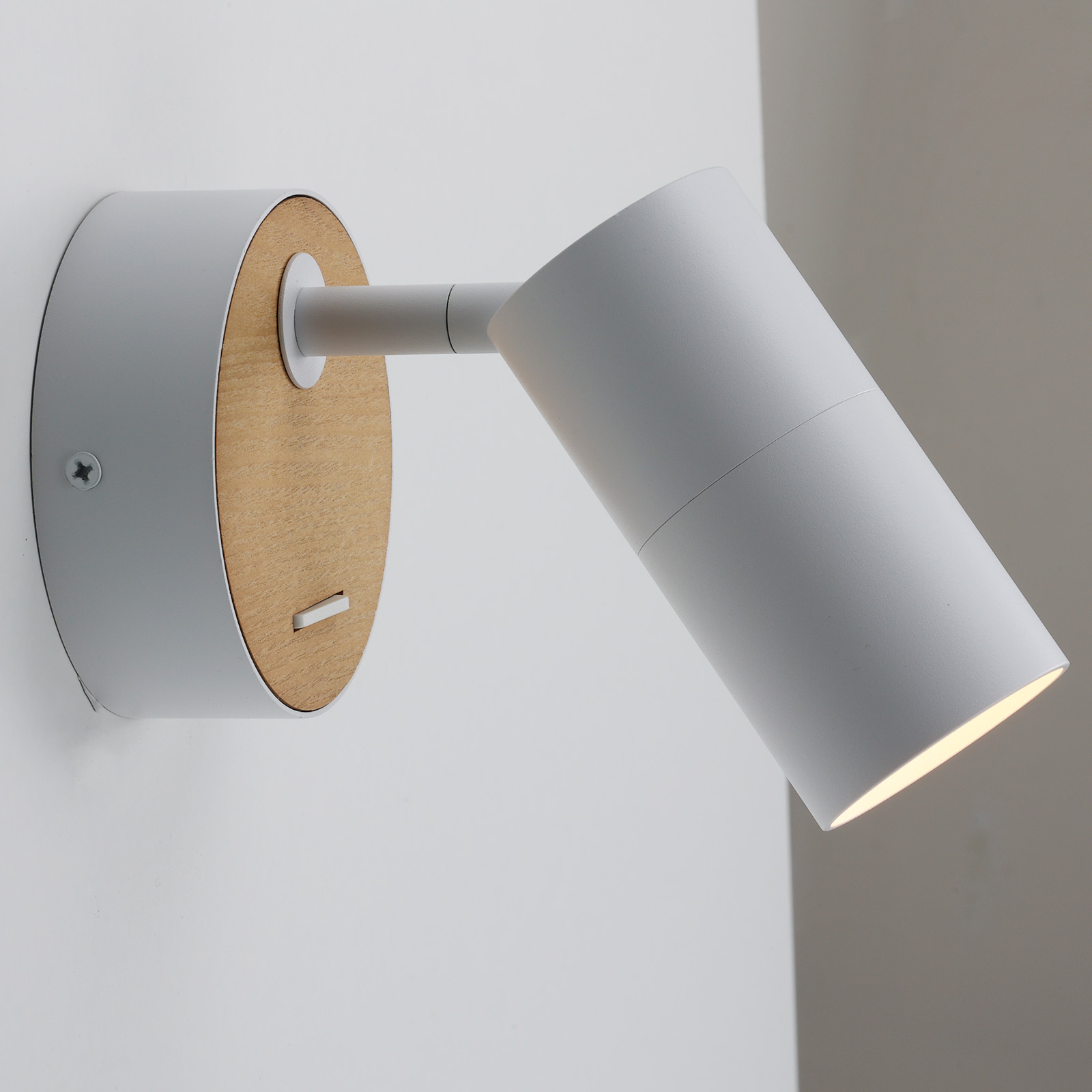 Lámpara blanca de pared con base de madera. La lámpara está en ángulo. El fondo es blanco.