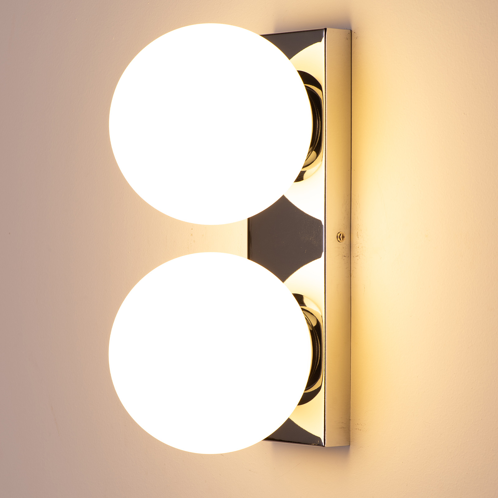 Una lámpara de pared con dos pantallas esféricas blancas y brillantes. La lámpara está montada en una pared.