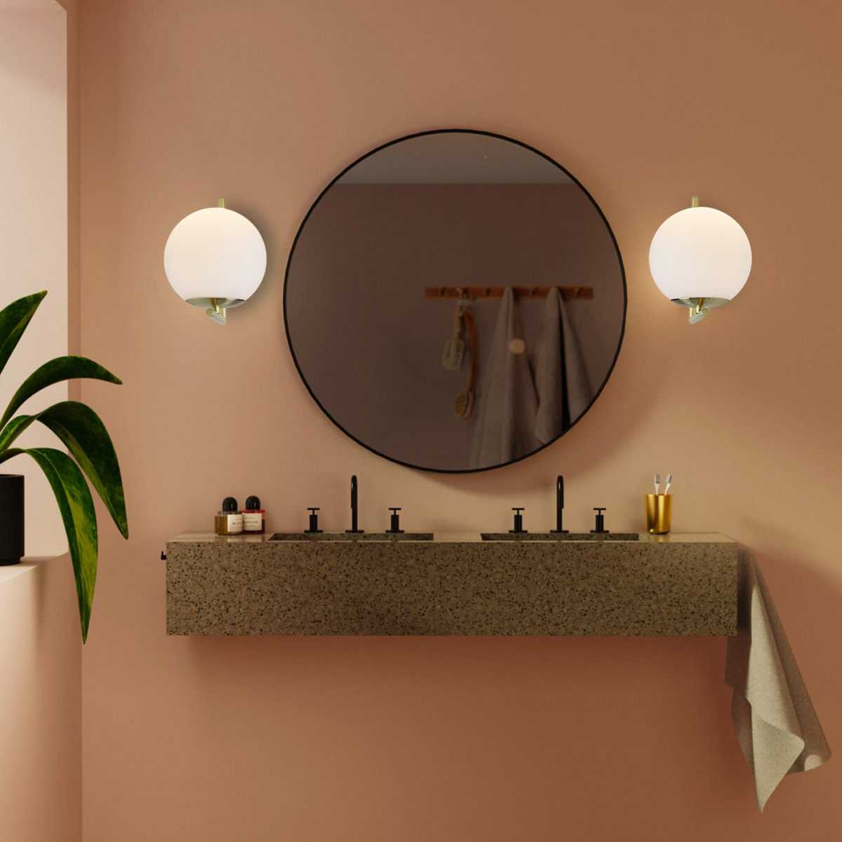 Una escena de baño con un gran espejo redondo, dos lámparas de pared esféricas, un lavabo doble y una toalla.