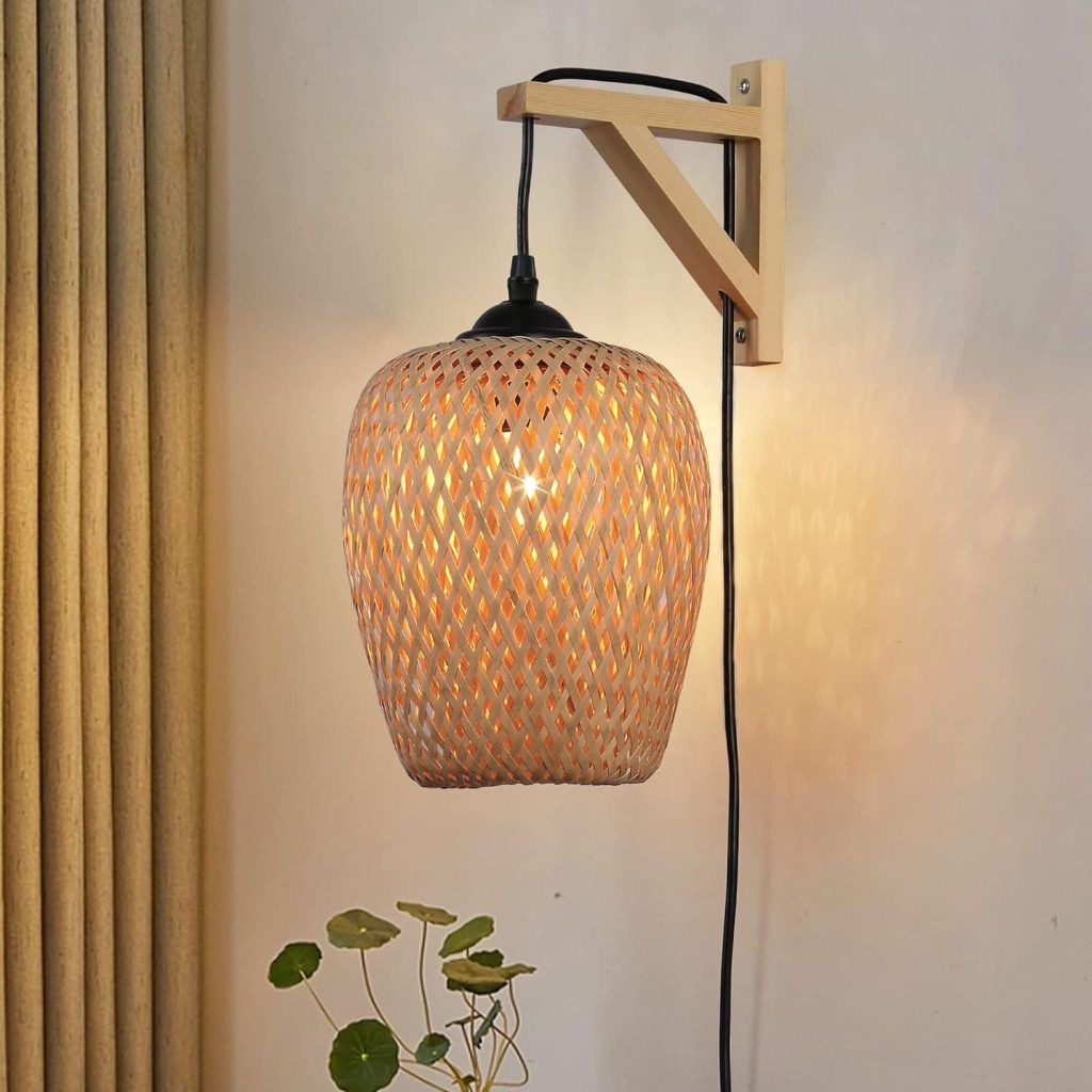 Una lámpara tejida cuelga de un soporte de madera en una pared beige, con cable negro y planta debajo.