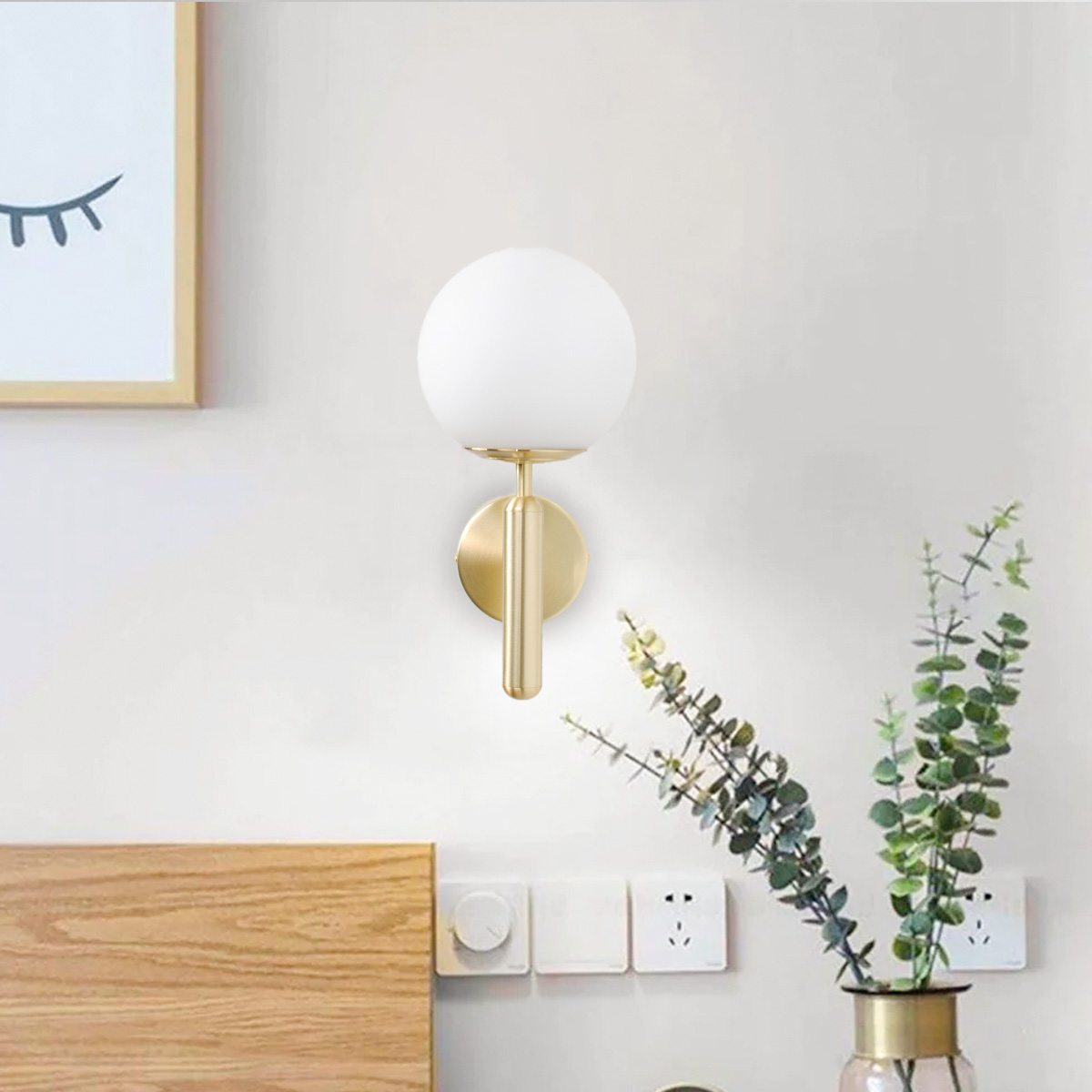 Una lámpara de pared dorada con un globo blanco y una planta en el fondo.