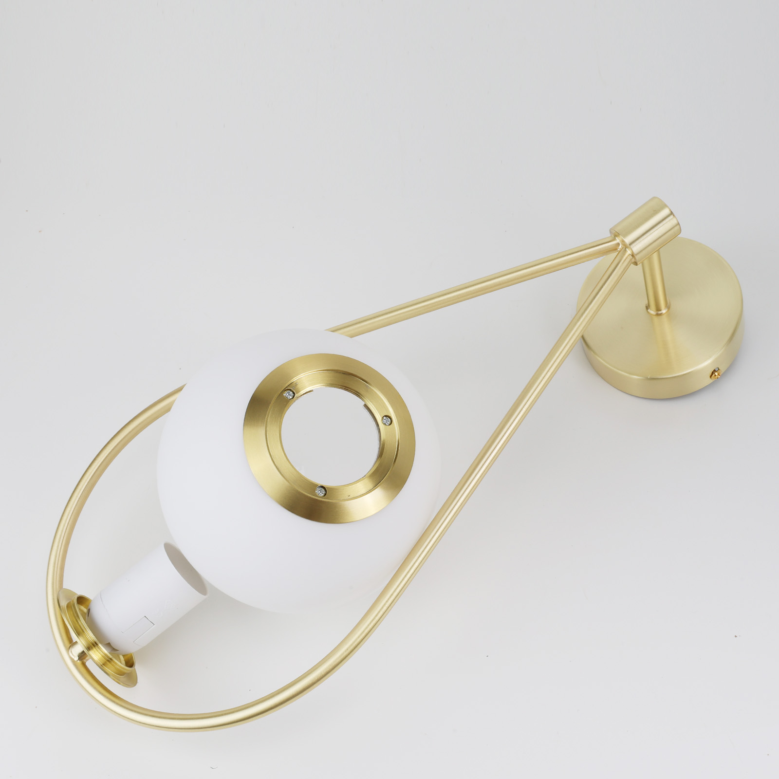 Una lámpara de pared con una bombilla blanca dentro de un marco dorado. Es en forma de lágrima con la parte inferior abierta.