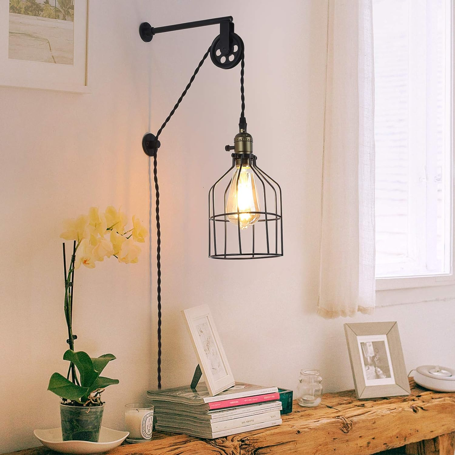 Lámpara de pared con sistema de polea, negro y dorado, con lámpara estilo jaula y bombilla expuesta.