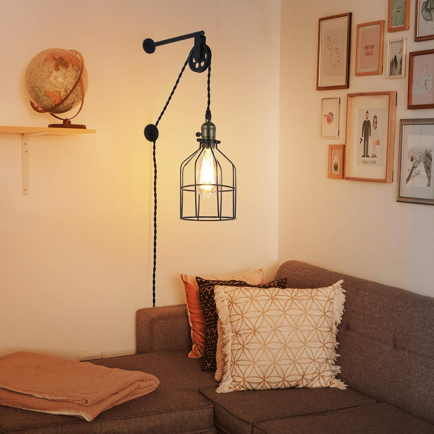 Lámpara de pared con sistema de polea, negro y dorado, con lámpara estilo jaula, en pared de sofá.