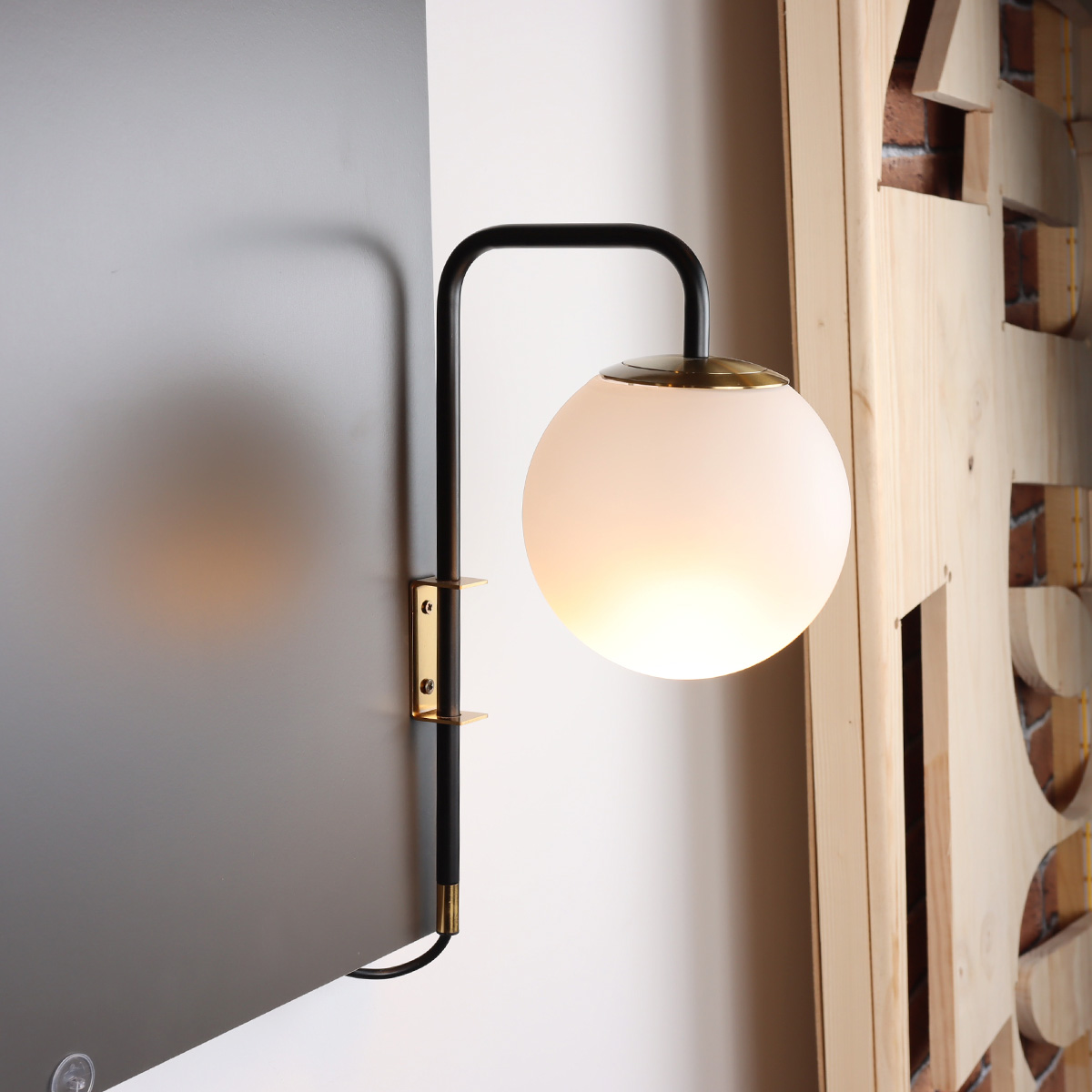 Una lámpara de pared con brazo negro y globo blanco, montada sobre una superficie gris junto a paneles de madera.