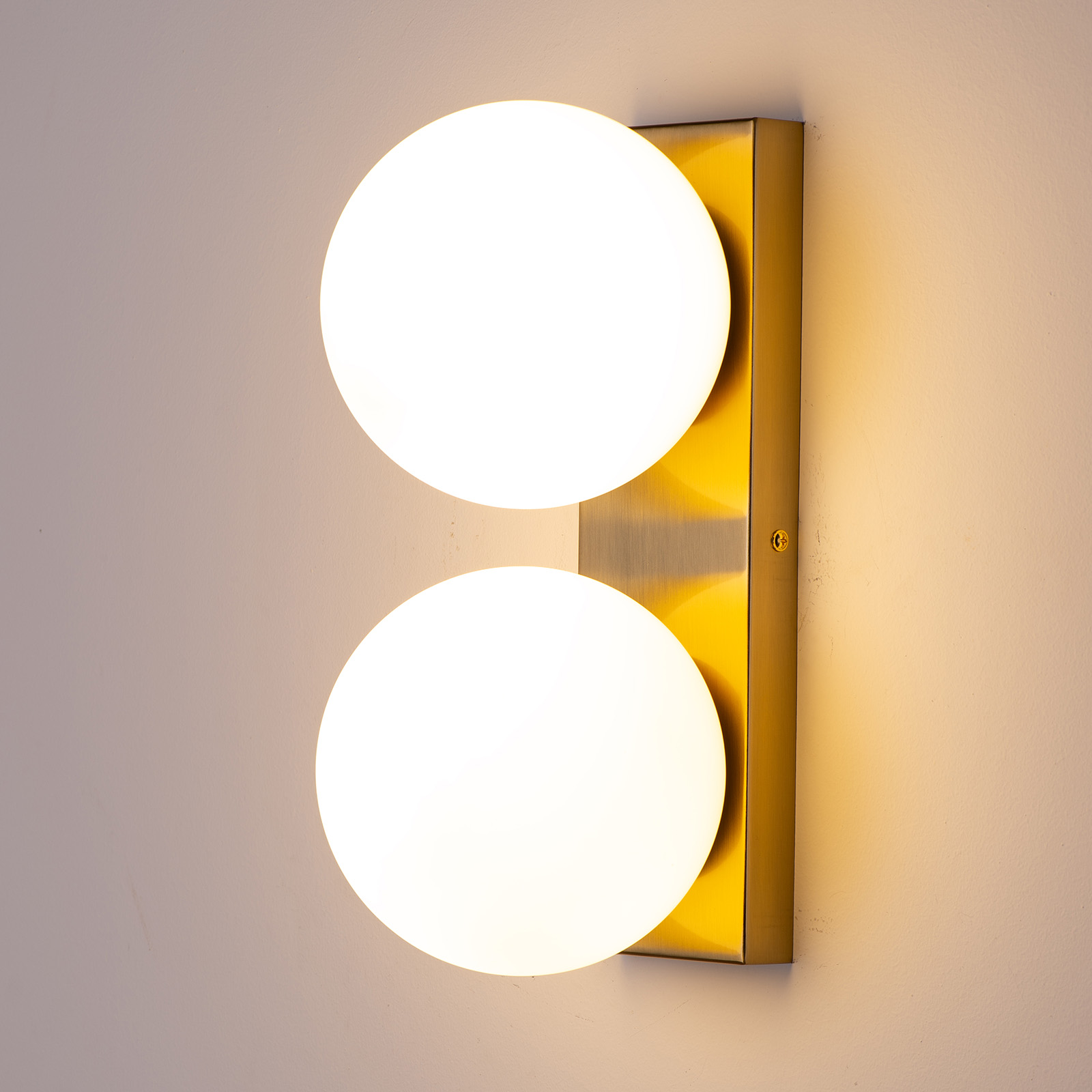 Dos bombillas redondas y blancas están alineadas verticalmente en un soporte de pared rectangular dorado.
