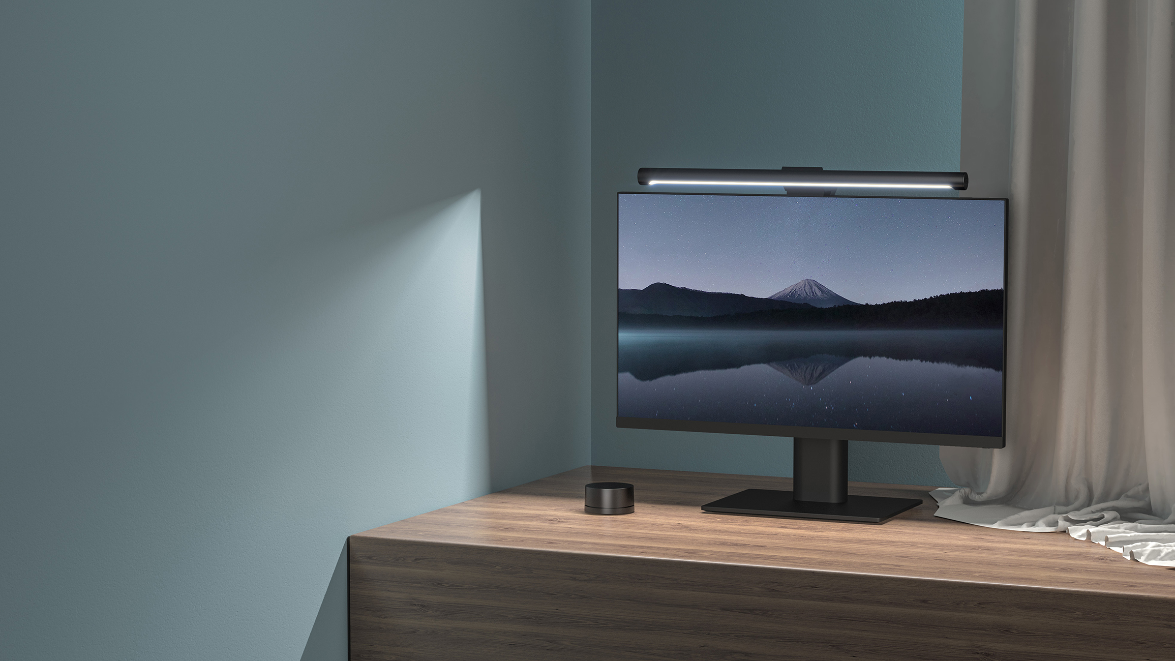 Monitor z górskim krajobrazem. Listwa świetlna u góry. Mały głośnik na biurku.