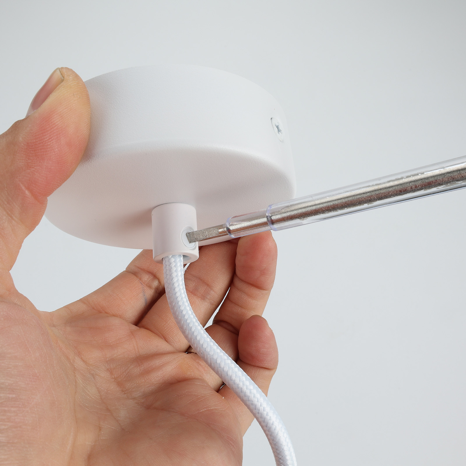 Una mano usando un destornillador para fijar el accesorio de una lámpara colgante blanca.
