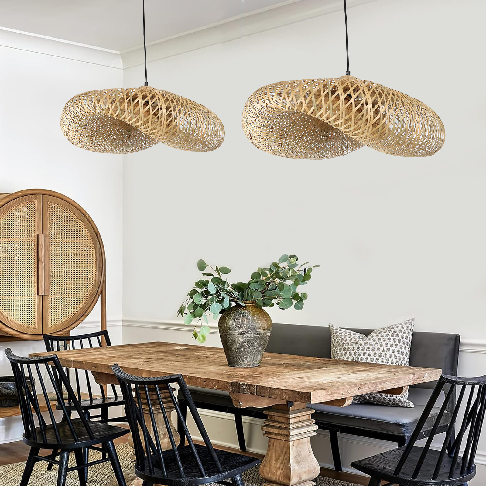 Dos pantallas de lámpara tejidas cuelgan sobre una mesa de comedor de madera, con sillas negras y un jarrón con ramas verdes.