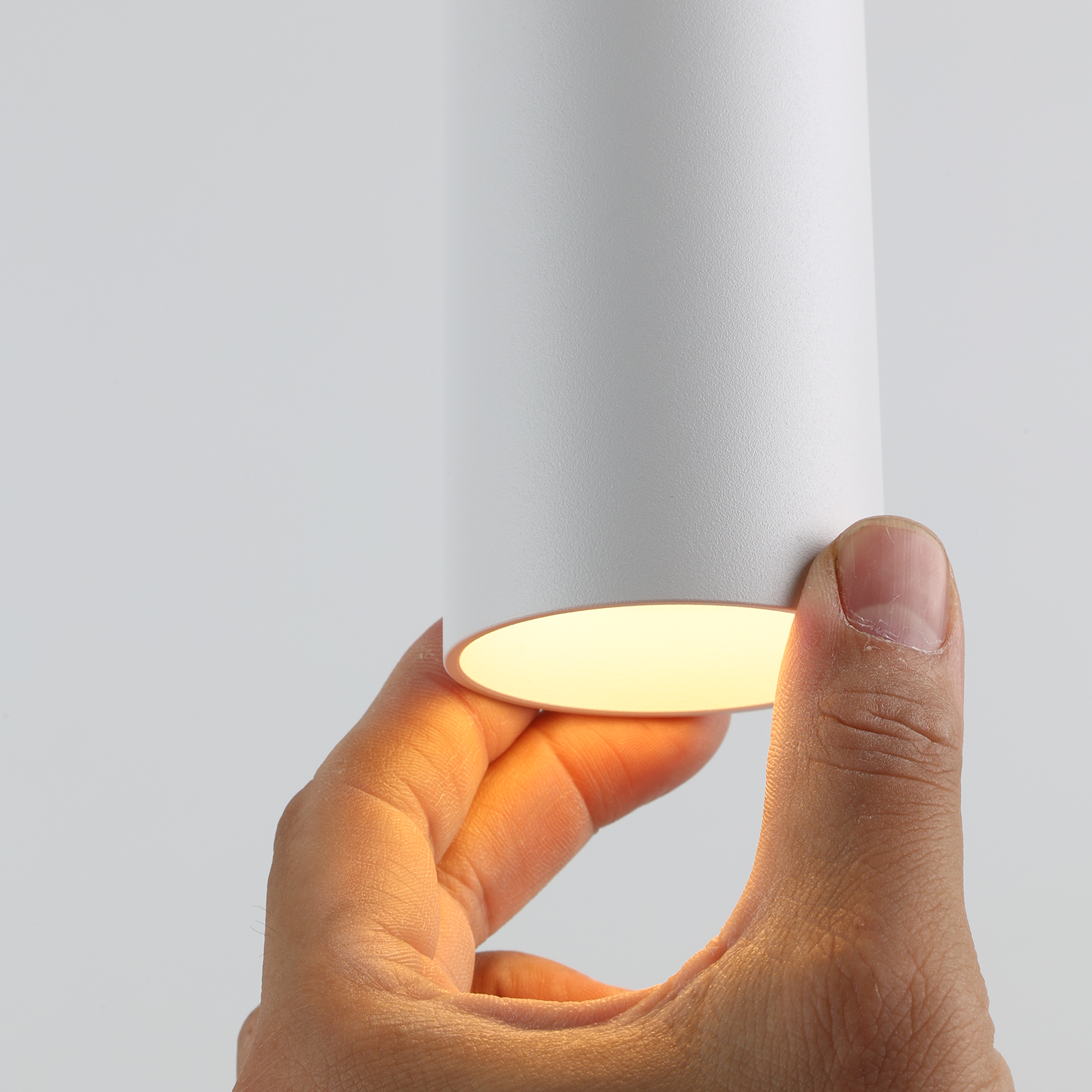 Una mano sosteniendo la parte inferior de una lámpara colgante blanca con luz brillando.