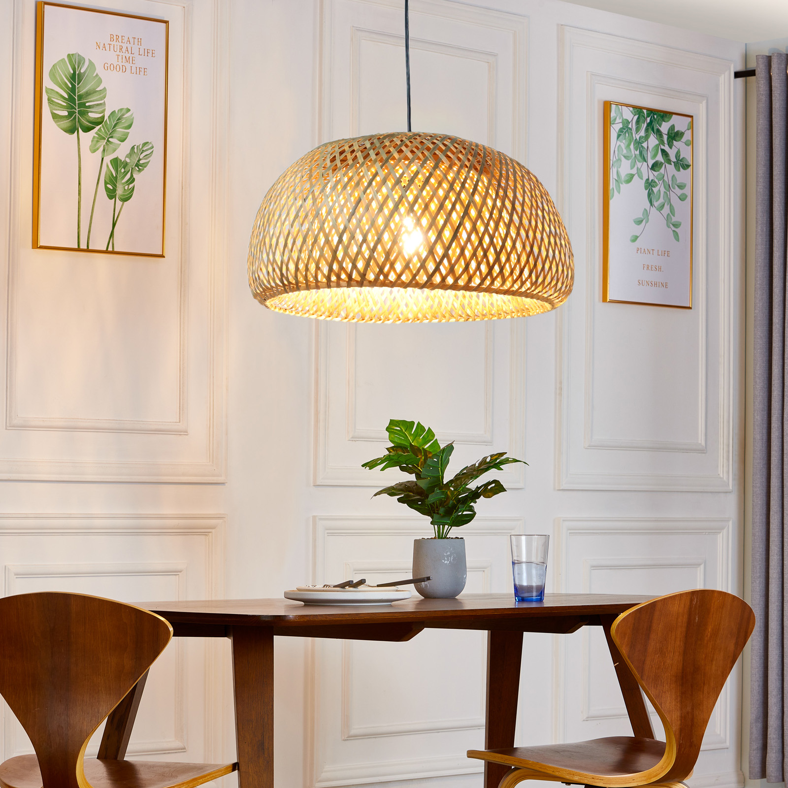Una lámpara colgante tejida cuelga sobre una mesa de comedor con sillas. También se ve arte y una planta.