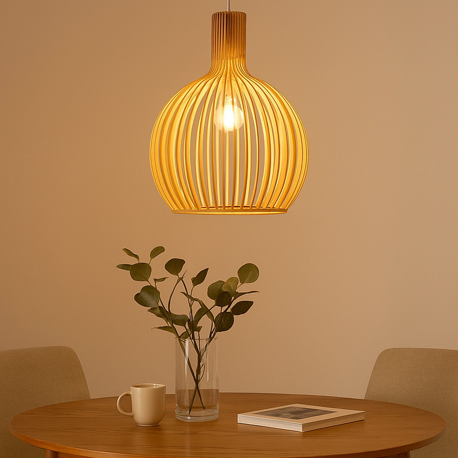 Lámpara de madera colgando sobre una mesa. Un jarrón con plantas y un libro en la mesa.