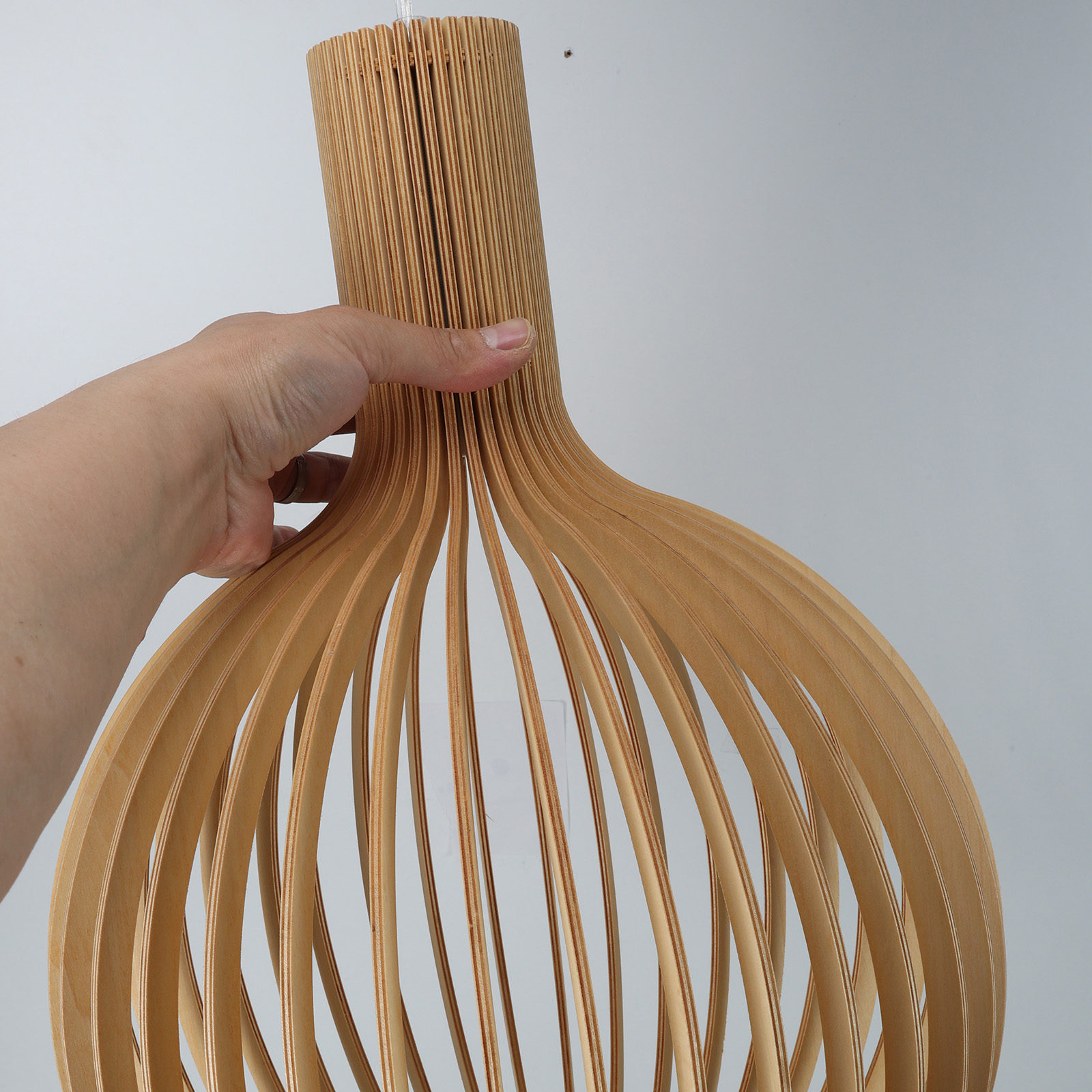 Una mano sosteniendo una lámpara de madera. La lámpara está hecha de listones de madera.