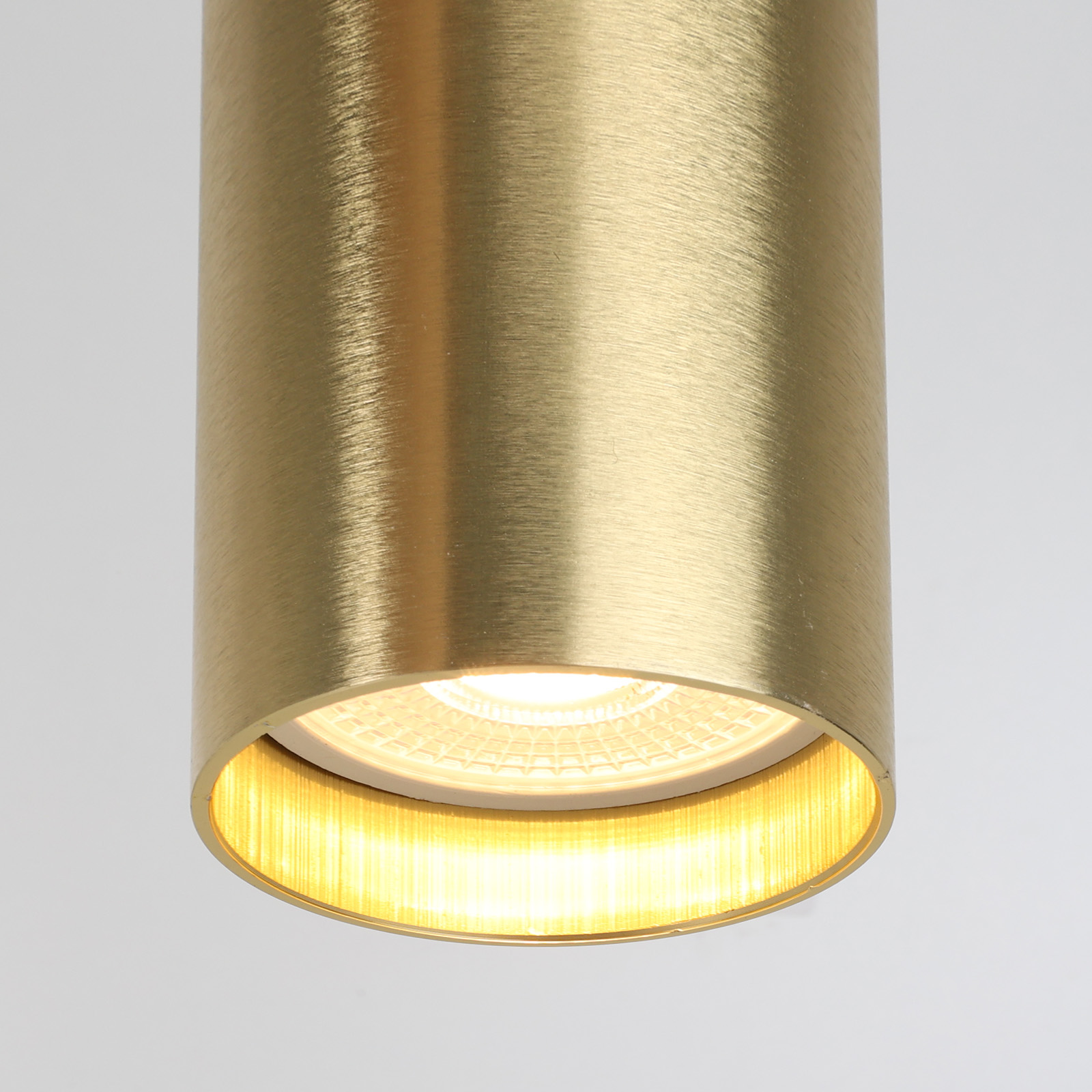 Un primer plano de una lámpara colgante cilíndrica dorada. La luz brilla a través de un patrón circular.